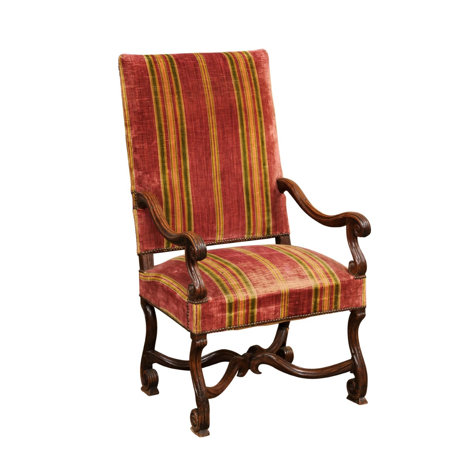 A French Louis XIV style carved walnut fauteuil from the late 18th century with large scrolling open arms, Flemish scroll legs, curving X-form stretcher and old upholstery. Created in France during the last decade of the 18th century, this armchair
