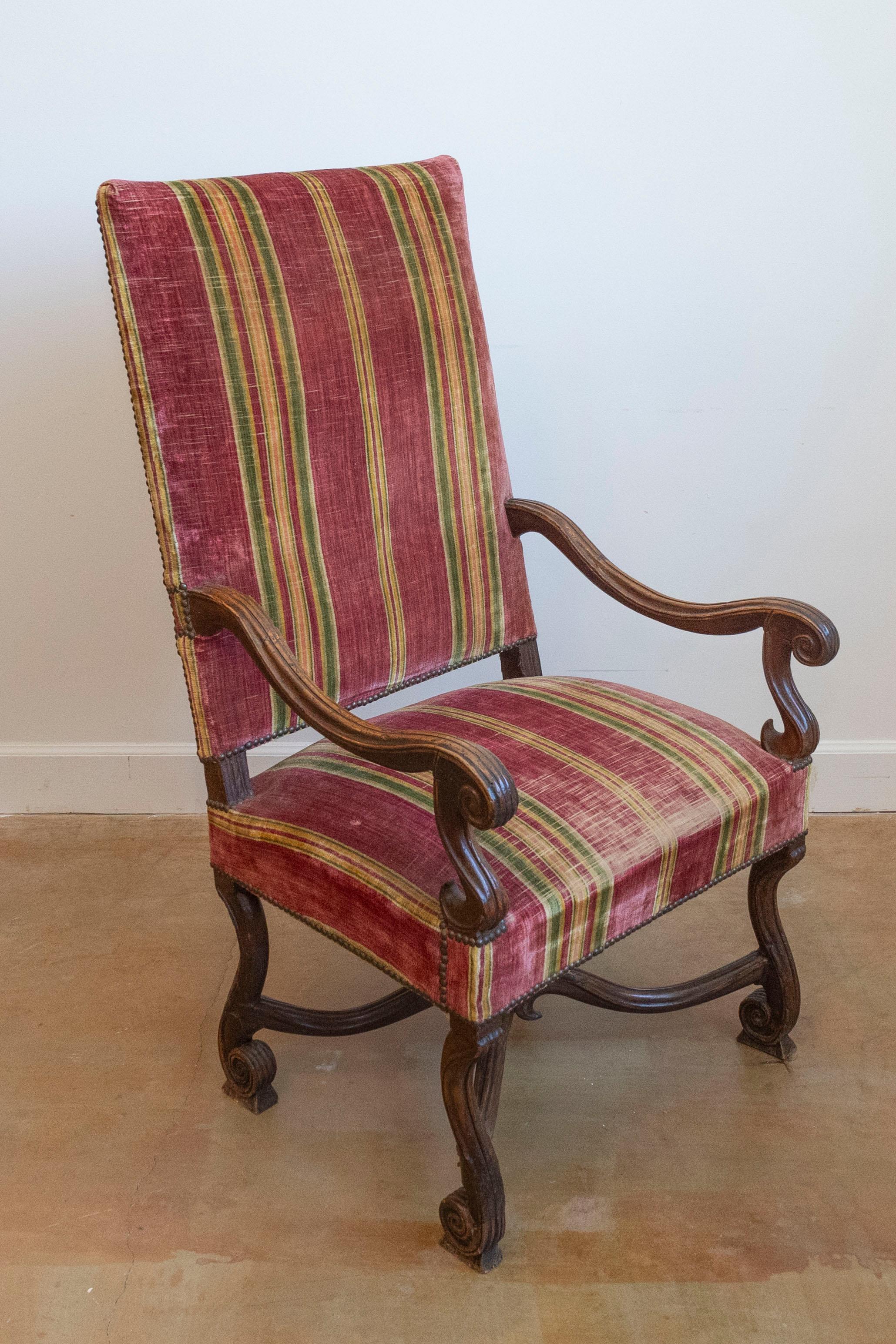 Fauteuil francés de nogal tallado, estilo Luis XIV, de finales del siglo XVIII, con grandes brazos abiertos en forma de volutas, patas de volutas flamencas, camilla curvada en forma de X y tapicería antigua. Creado en Francia durante la última