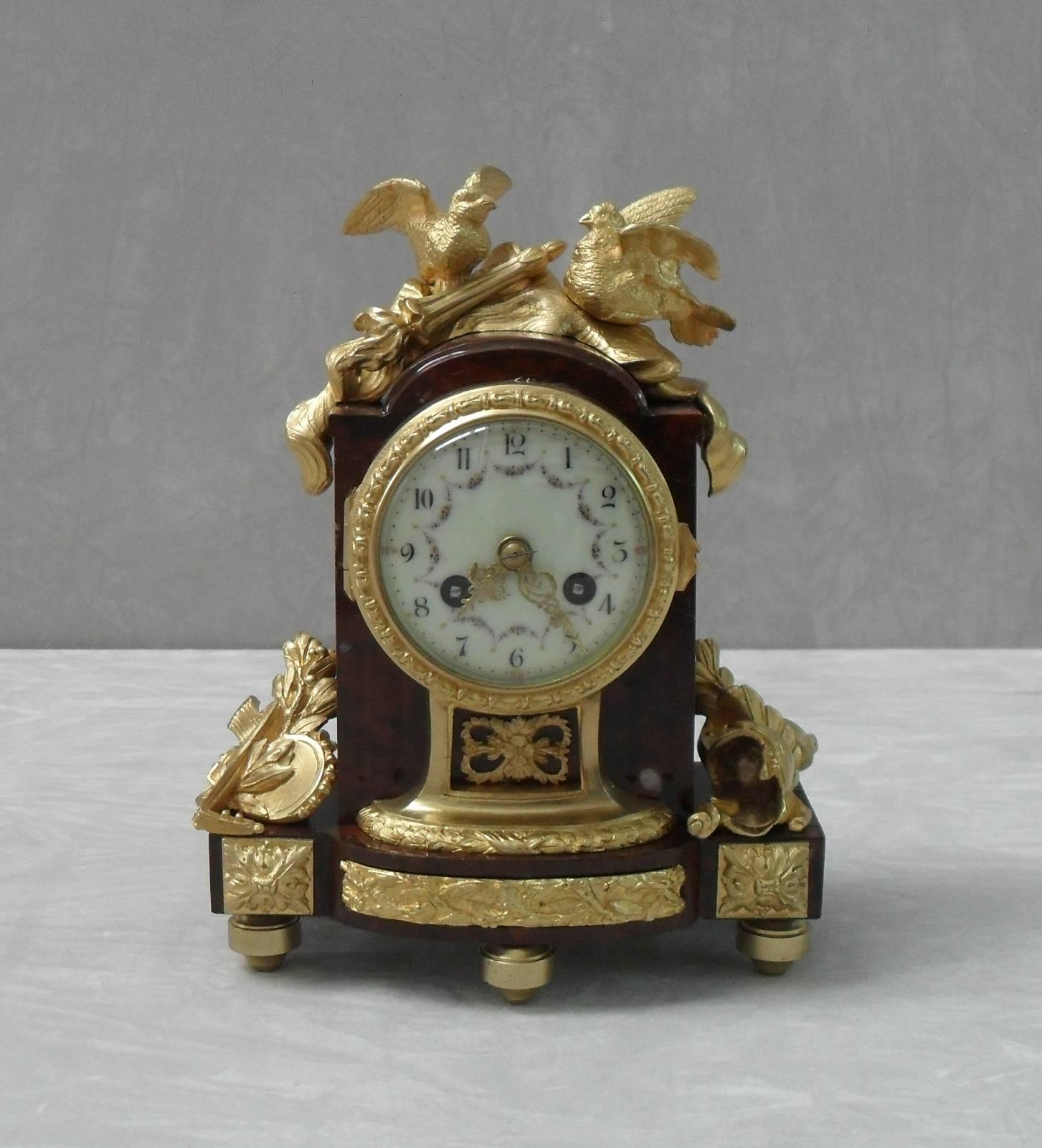 An extremely fine quality French Louis XIV style deep rouge marble and bronze gilt clock set comprising of a pair of two branch candelabra garnitures and a mantel clock. The clock is adorned with musical instruments, soldiers helmet, shield and is