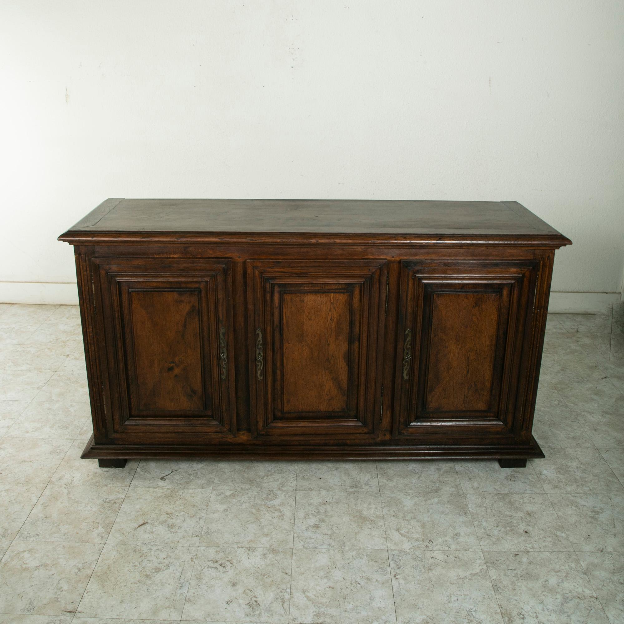 This French Louis XIV style oak enfilade or sideboard from the turn of the twentieth century features hand pegged paneled sides and doors, and a beveled top. Its three doors display Louis XIV design elements with symmetrical diamond point