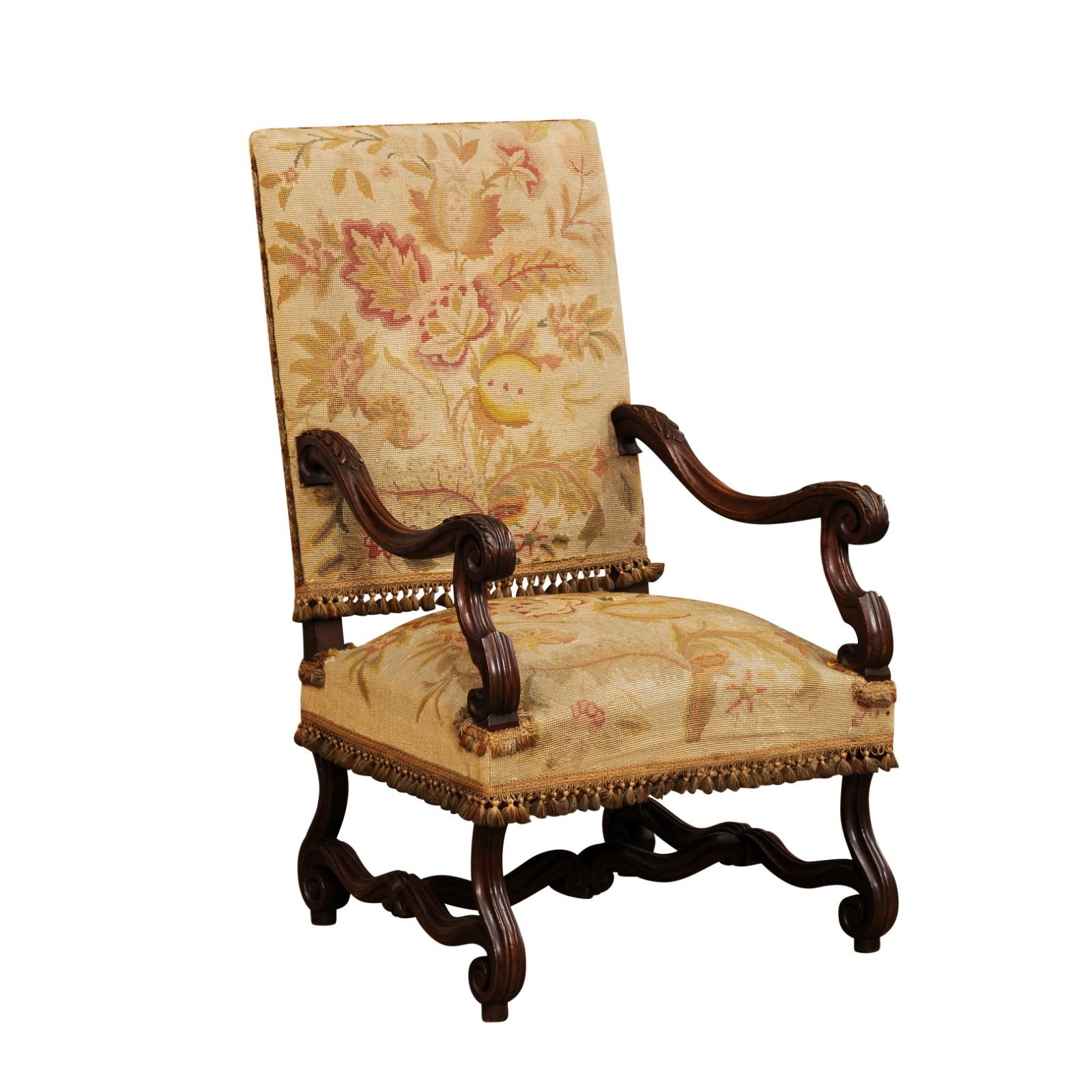 A French walnut Louis XIV style armchair from the 19th century with rectangular slanted back, large scrolling arms, carved acanthus leaves motifs, scrolling legs and carved cross stretcher. Introduce a touch of opulence to your interiors with this