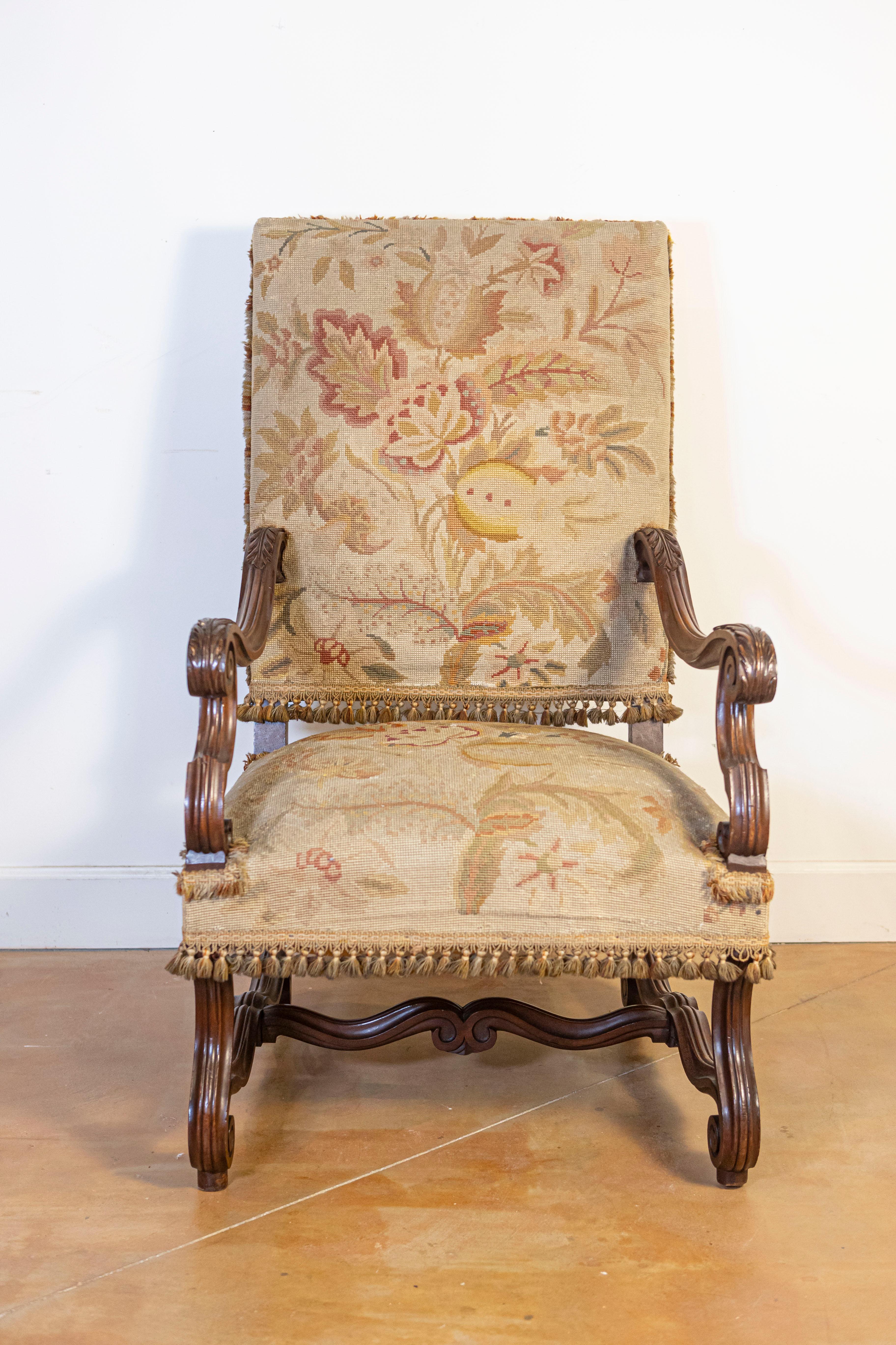 Sillón francés de nogal del siglo XIX, estilo Luis XIV, con respaldo rectangular inclinado, grandes brazos en forma de roleo, motivos de hojas de acanto talladas, patas en forma de roleo y cruceta tallada. Introduce un toque de opulencia en tus