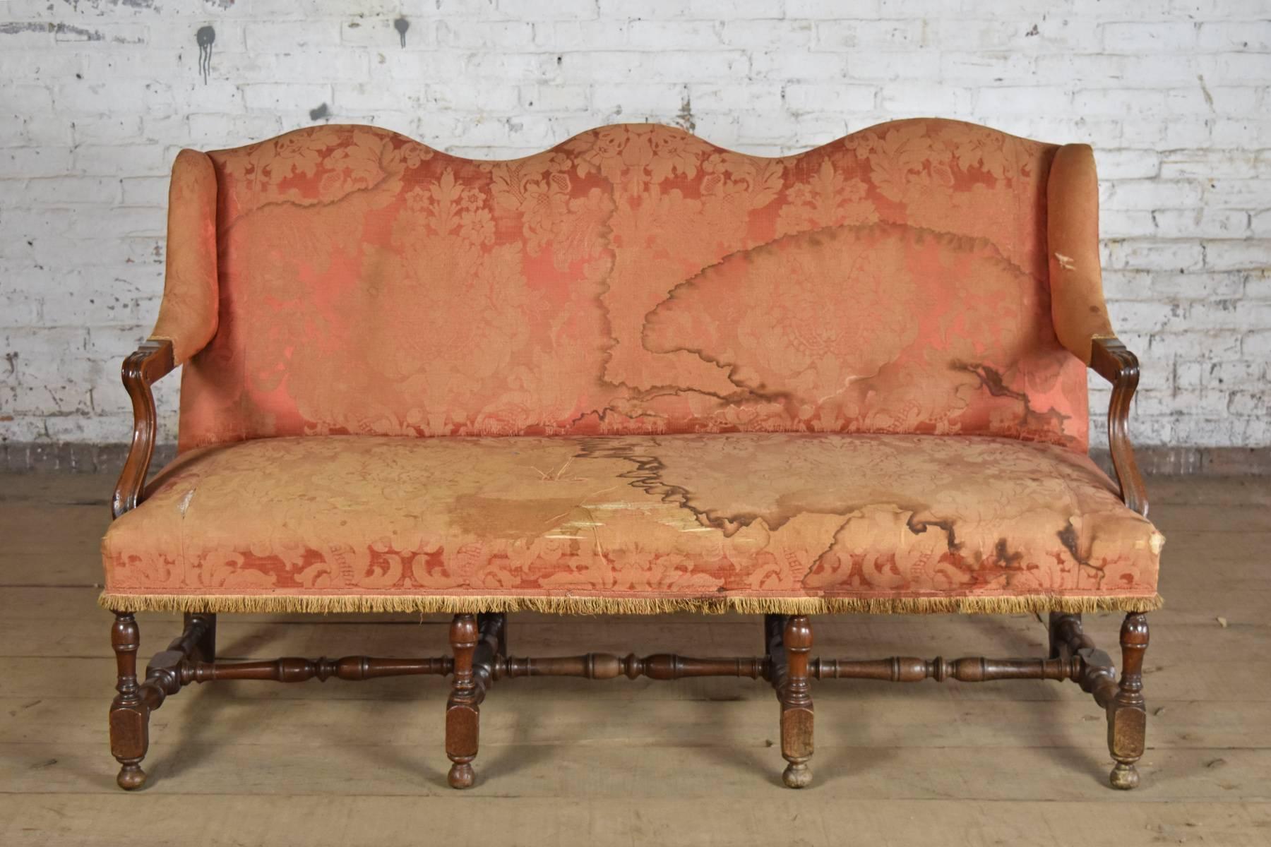 A settee of small size, elegant lines and understated details, triple-arch-back, open scrolling arms, the seat supported by four turned front legs connected by turned center stretchers to the corresponding chamfered back legs. Pegged
