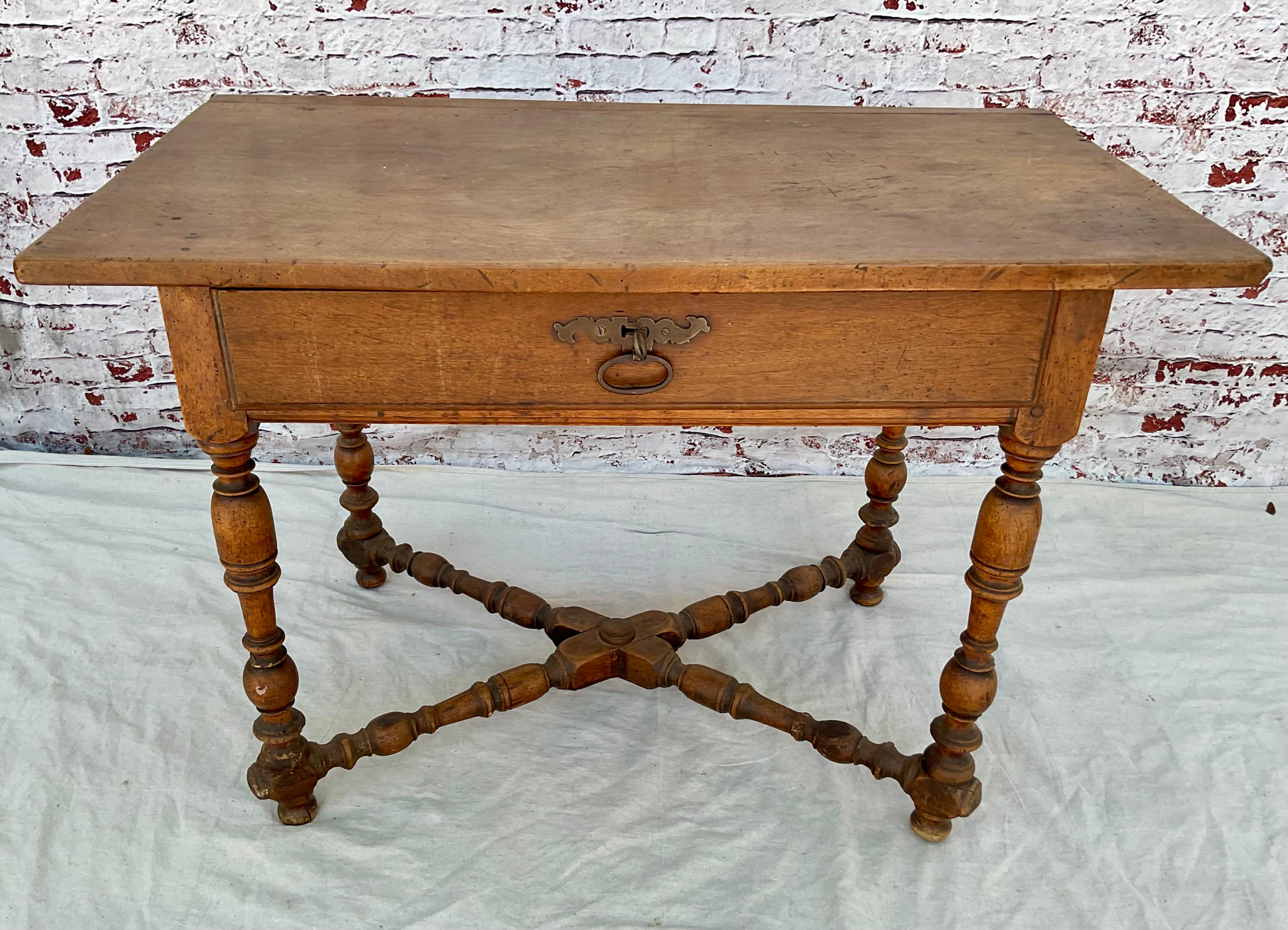 Charmante table en noyer Louis XIV du XVIIIe siècle à plateau rectangulaire mouluré. La table comporte un long tiroir en freize avec une tirette centrale en fer forgé et des pieds tournés reliés par une entretoise en X se terminant par des pieds en