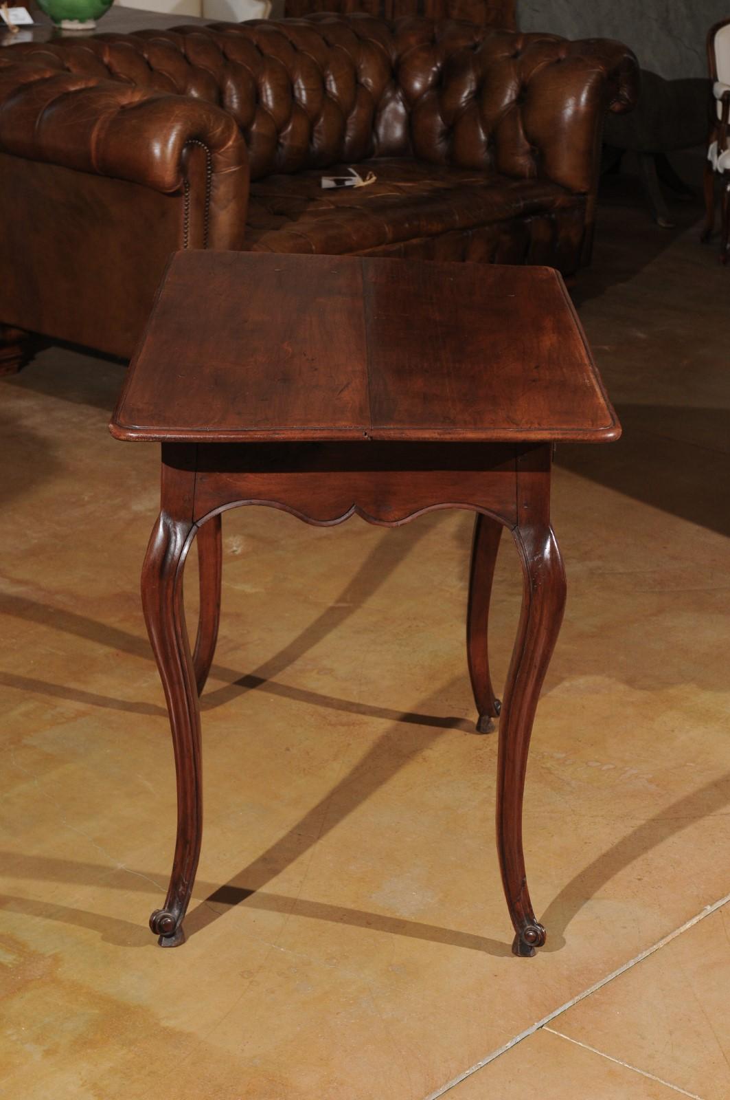 A French Louis XV period side table in solid walnut from the late 18th century, with single drawer, X-form fretted motifs, scalloped apron and cabriole legs. This French side table features a rectangular top with molded edges and rounded corners,