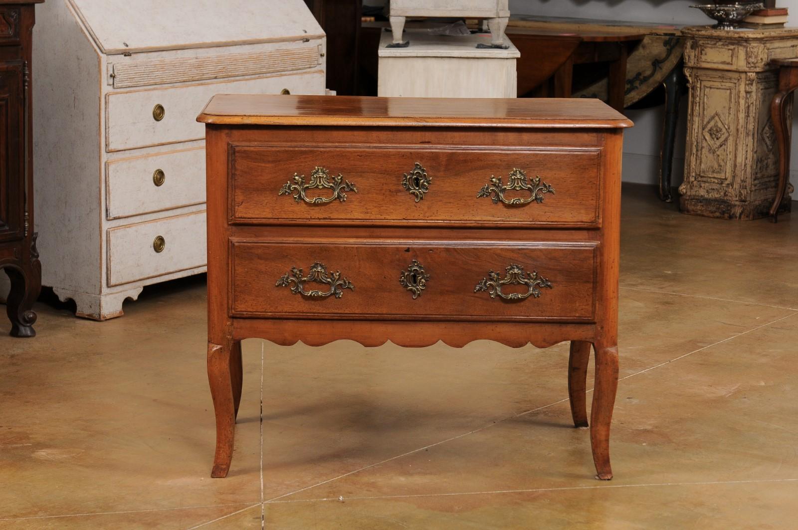 A French Louis XV walnut commode Sauteuse from the late 18th century, with two drawers, bronze Rococo hardware, cabriole legs and small proportions. Created at the end of the reign of France's last absolute monarch Louis XVI's in the last decade of