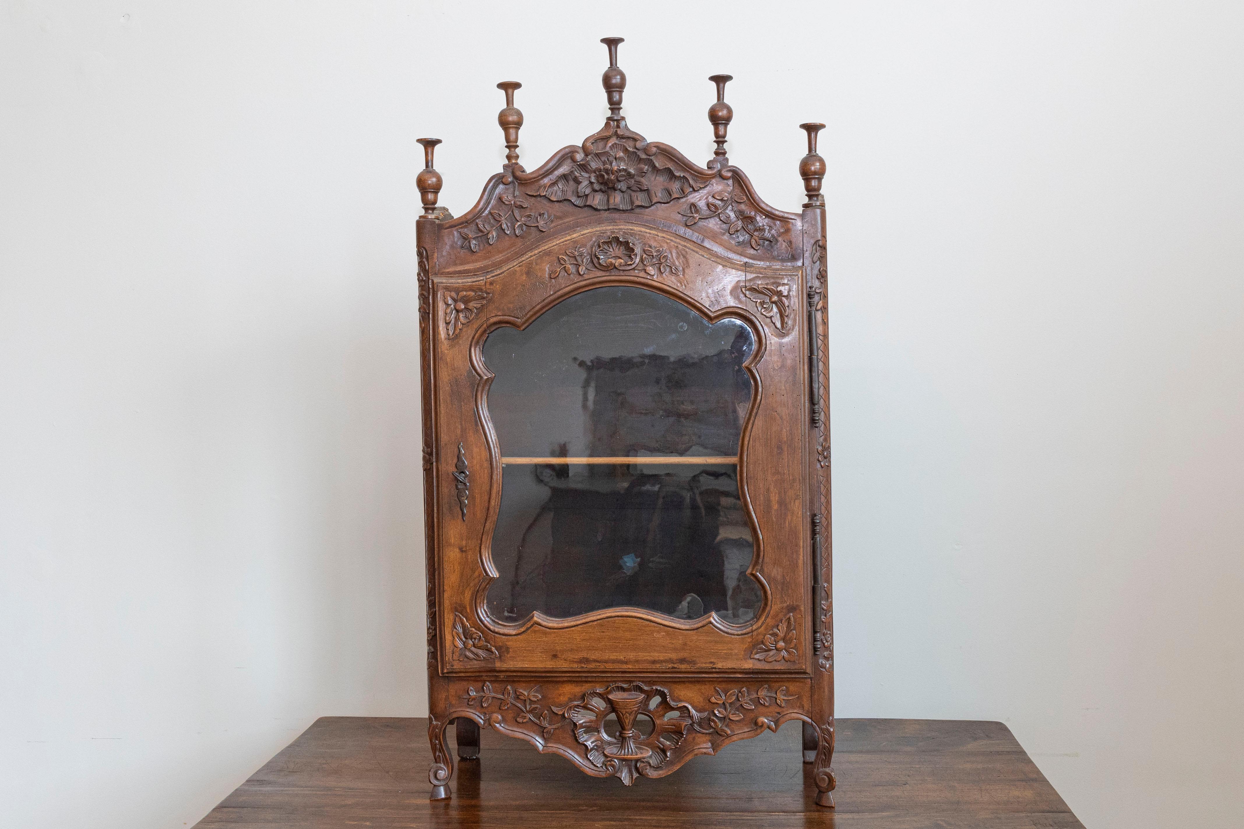 Piccola vetrina francese in noce di epoca Luigi XV del XVIII secolo, con un'unica anta in vetro e motivi floreali riccamente intagliati. Creata in Francia nel XVIII secolo, questa piccola vetrina in noce Luigi XV è caratterizzata da un piano a