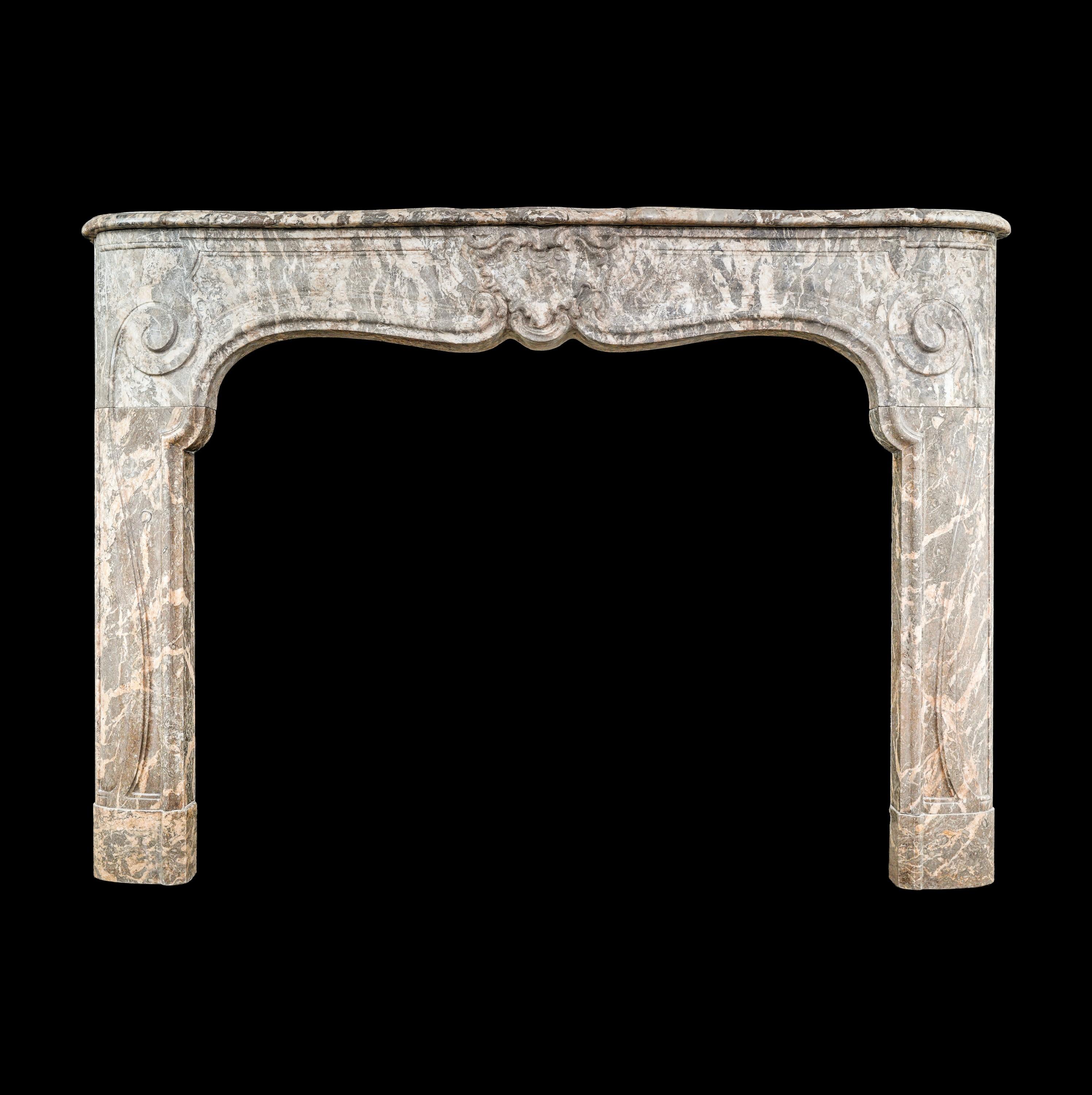 A harmonious palette of gray, light brown, and tan hues blend together to create an inviting, earthy ambiance in this Louis XV marble mantel. Its design is truly distinctive, featuring gracefully curved lines that ascend from rounded plinths into