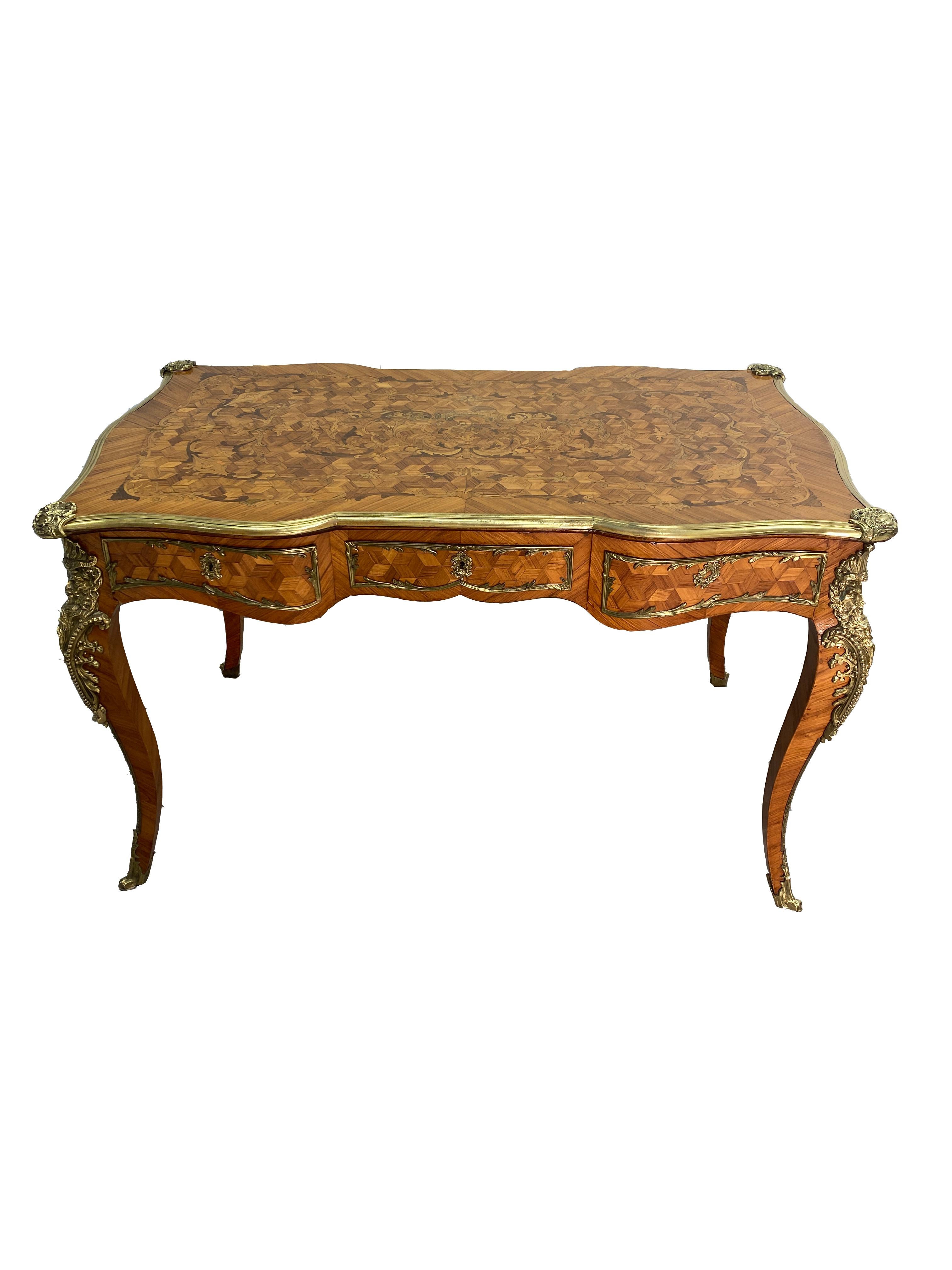 This is a handsome French Bureau plat desk in Louis XV style, made in France Circa 1880. The desk is decorated highly with parquetry and marquetry inlay on the sides and top. The brass ormolu is highly polished throughout the desk. Three drawers