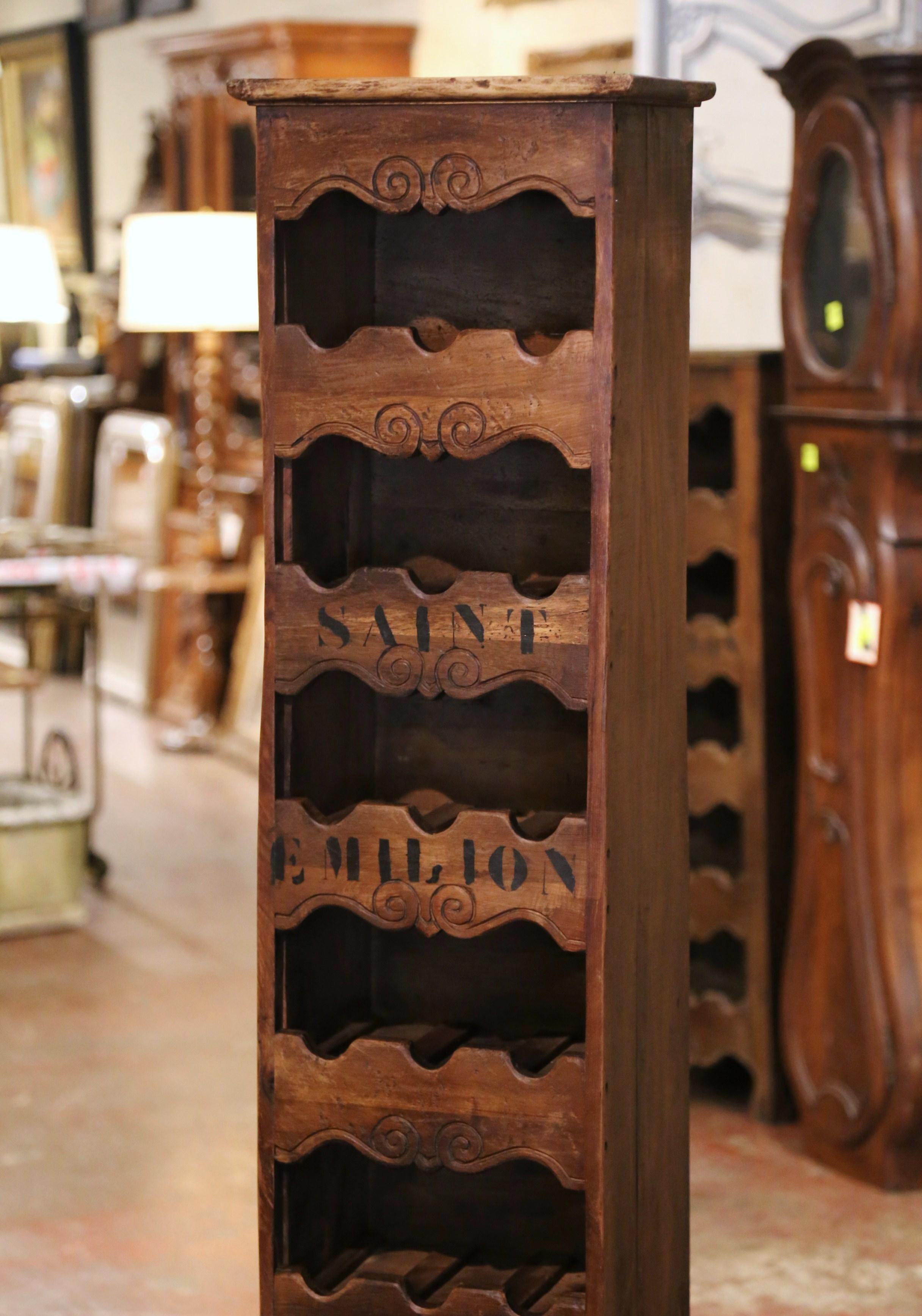 This narrow, antique wine storage cabinet was crafted in western France using old timber. Built of pine wood, the tall and thin cabinet sits on four small scroll feet under a scalloped apron. The piece features seven shelves embellished with