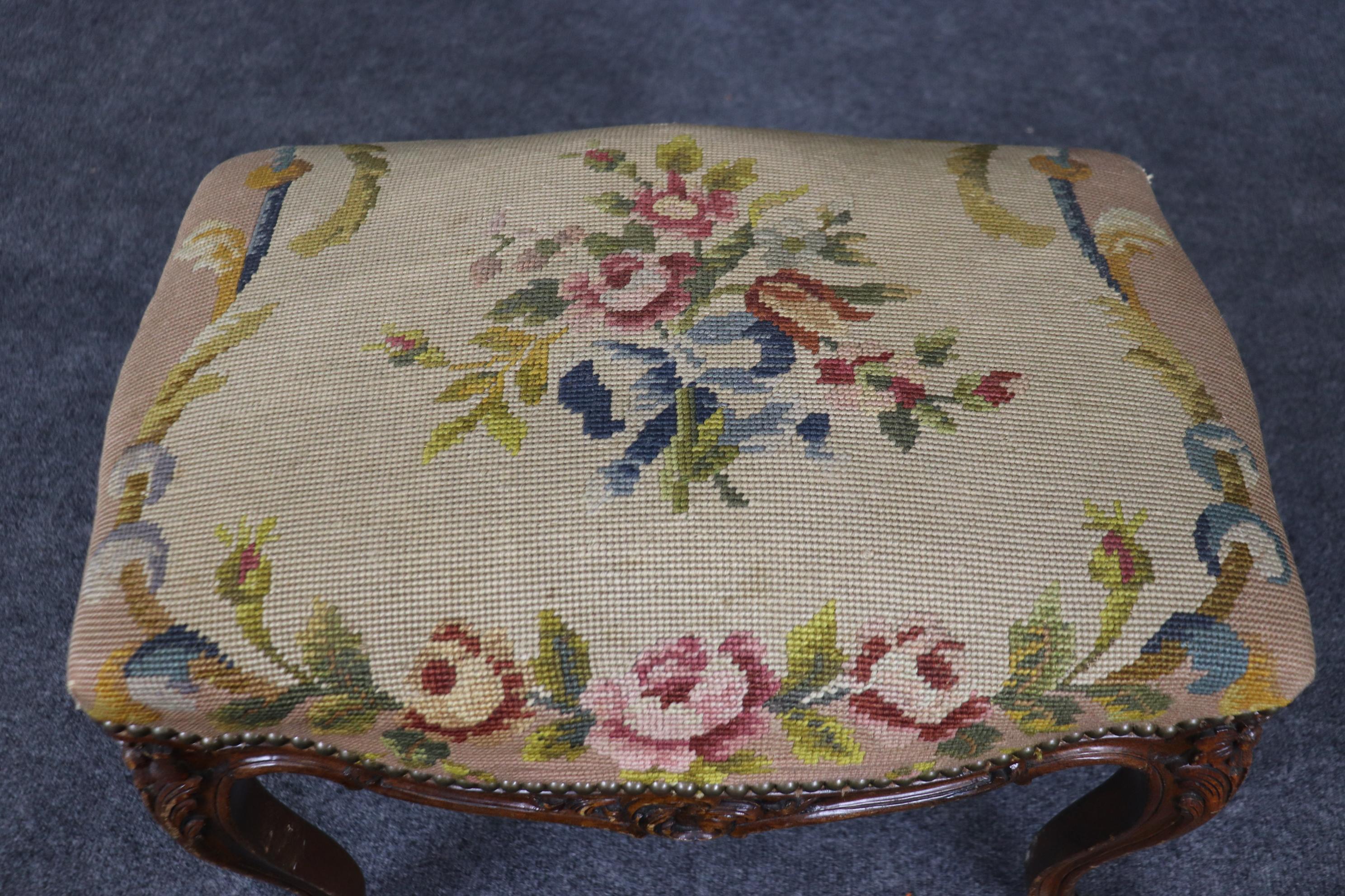This is a gorgeous French antique walnut foot stool with a gorgeous needlepoint upholstered seating surface. The stool is in antique distressed condition and will show parts of the base loose antique distressing to the frame and Measures 19.25 tall