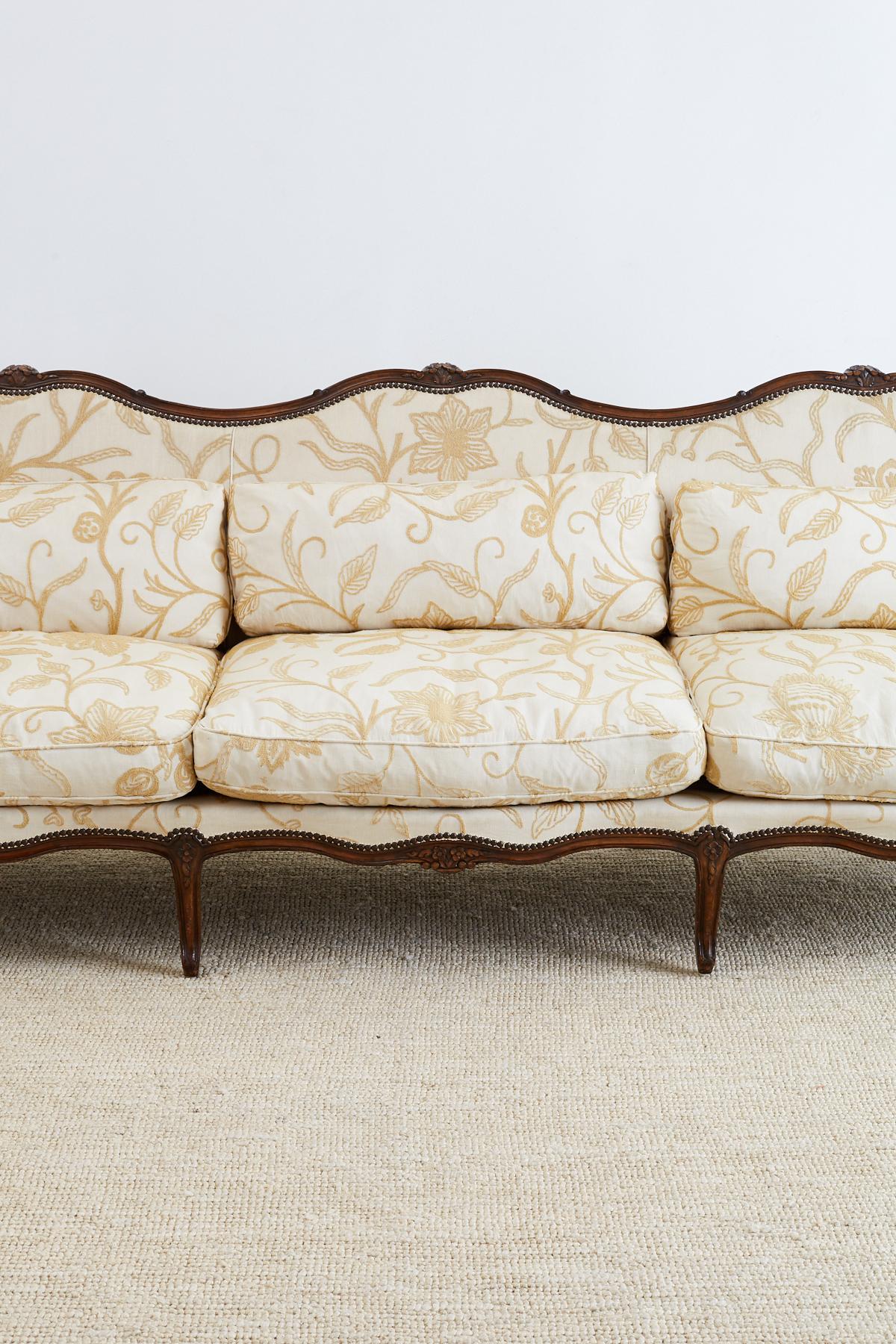 Grand French wingback sofa or canapé a oreilles made in the Louis XV taste. Features a large triple back hand carved walnut frame having a serpentine crest and seat. Restored and upholstered in the late 20th century with an impressive wool