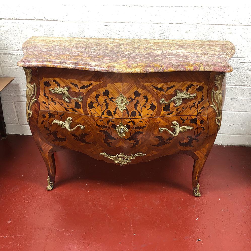 A fine French Louis XV serpentine bombay form sans traverse commode with a rare variegated marble serpentine shaped with a double carved ogee edge, the case with two shaped drawers marquetry inlaid king and tulip woods with floral motifs and leaves