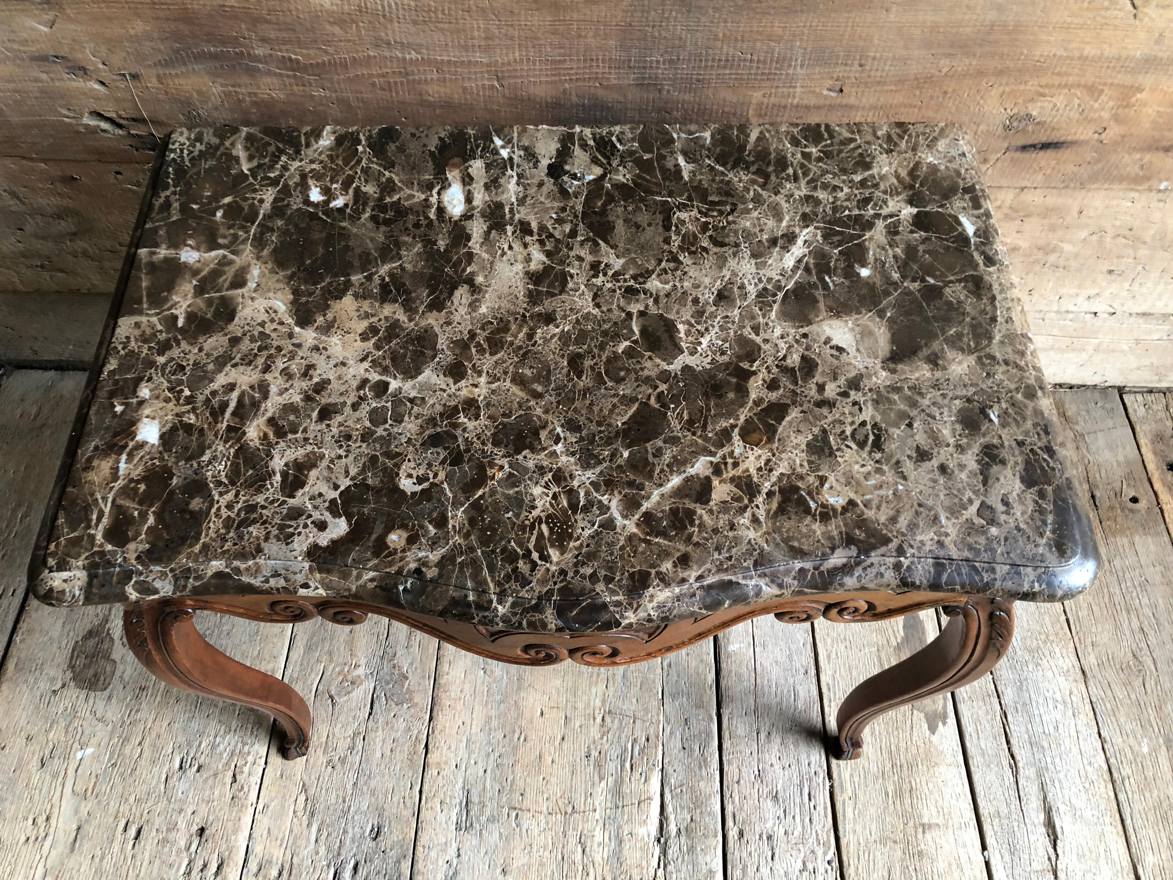 A French Louis XV period console table in walnut with a brown and white marble top (original) the base in a serpentine form with a scalloped apron, cabriole legs and pied de biche feet, nicely carved with acanthus leaves, scrolls and vines with