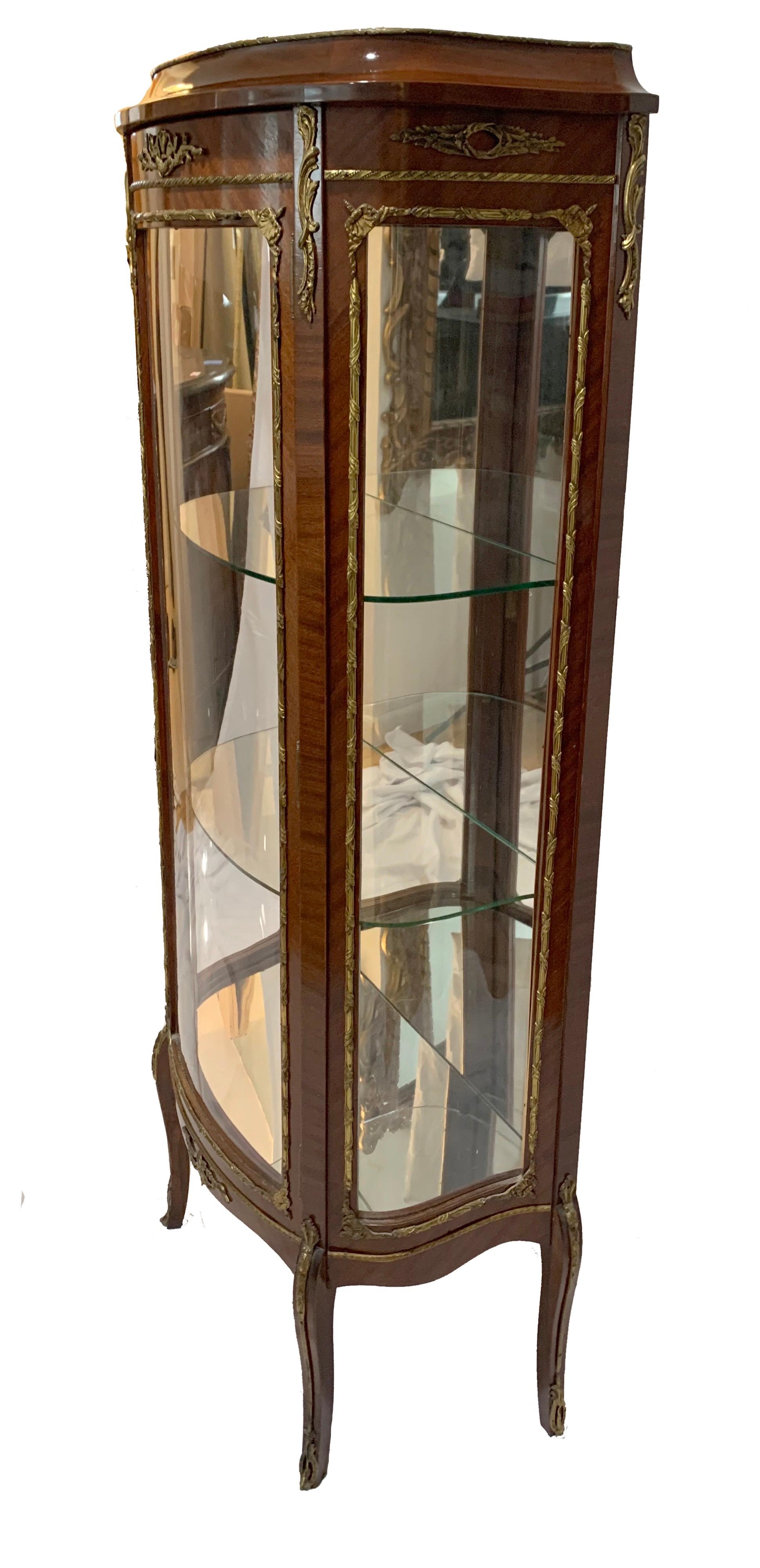 Exquisite French Louis XV display curio cabinet features intricate gilt bronze detail, three glass panels, mirrored glass interior backing, two curved glass shelves, curved single swing door and elegant French form.