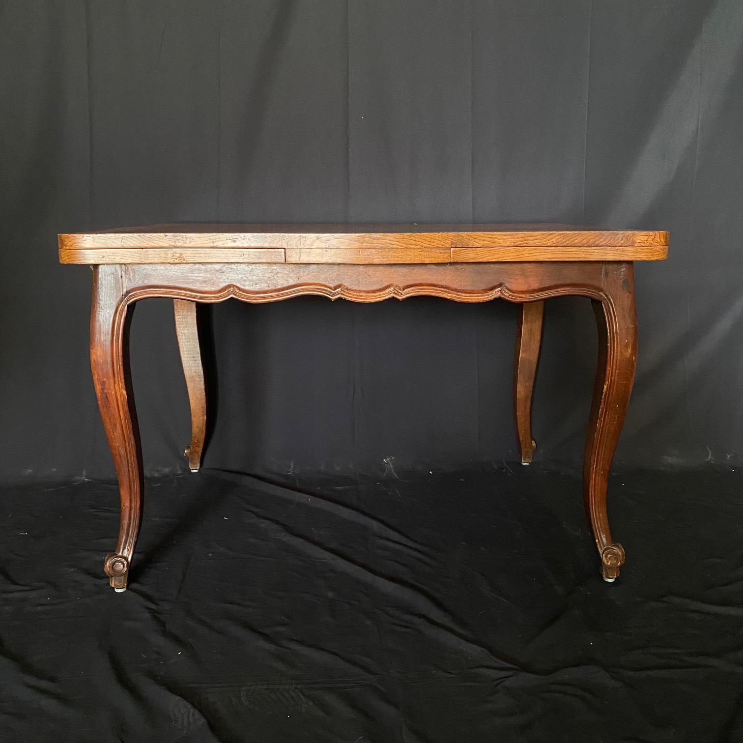 Elegante mesa de comedor provincial francesa Luis XV de roble macizo tallado, con un precioso tablero con incrustaciones a juego y dos hojas extraíbles, que tiene un precioso delantal tallado a mano y festoneado con volutas, todo ello sostenido por