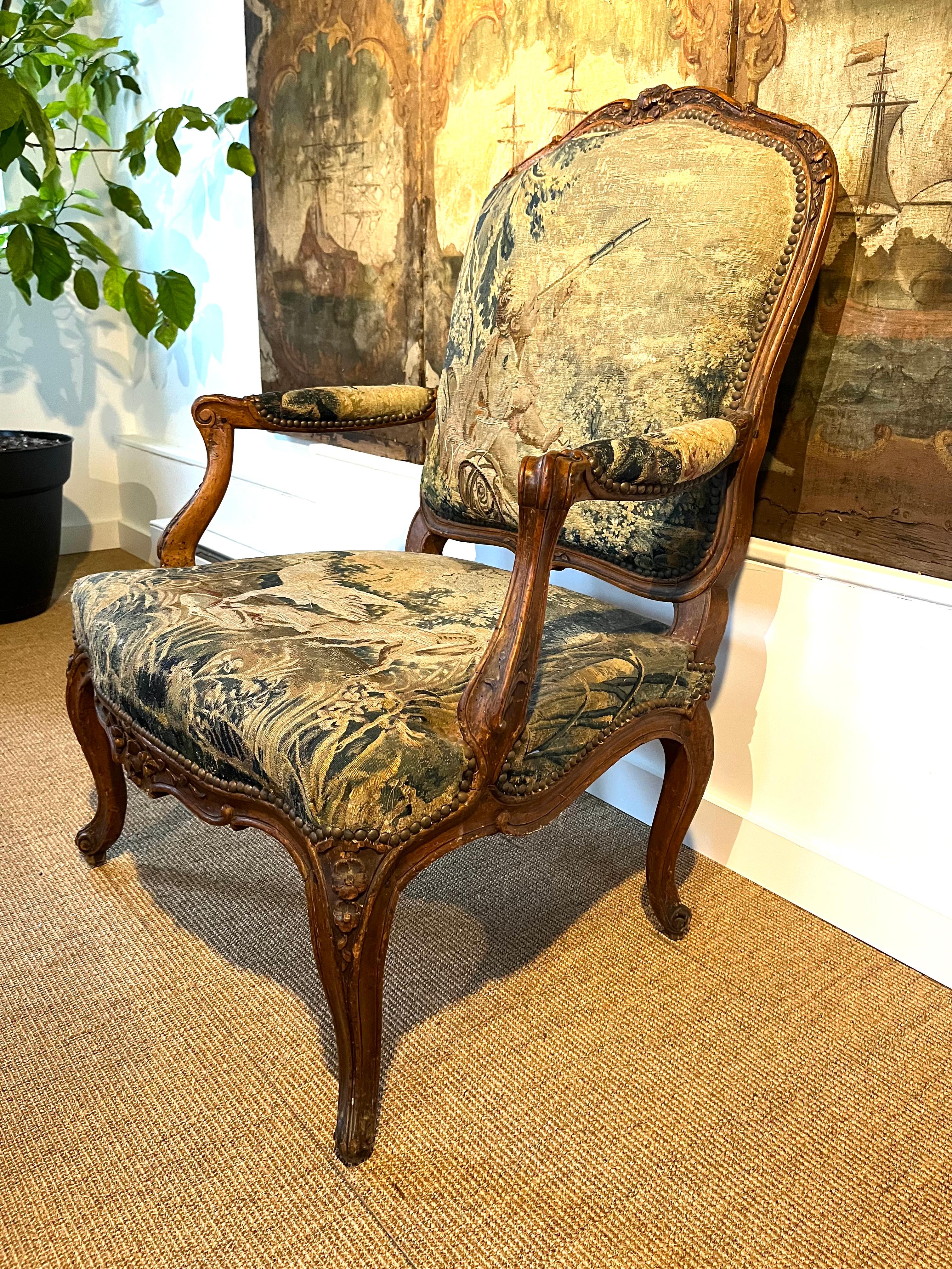 A fine Louis XV period fauteuil a la reine, stamped under seat rail “G.LEBRUN”, circa 1760, upholstered in its original Aubusson verdue tapestry depiction a child with a telescope and various animals, the frame in carved and stained beech. Nice