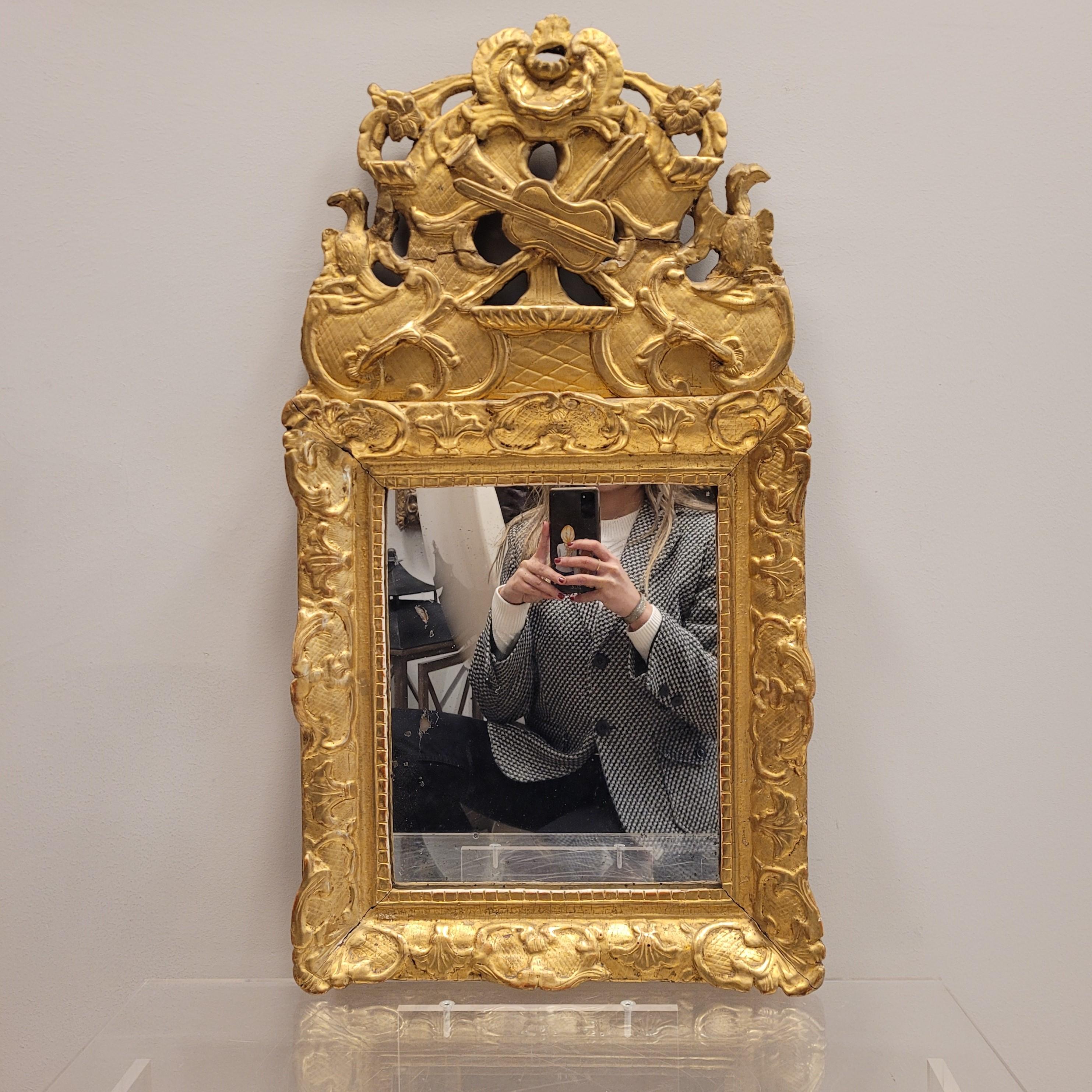  
One of a kind  French Louis Mirror wall, S XVIII,  , in carved and gilded wood .
The frame is crowned by an elaborate  central finial of carved and perforated gild wood, with decoration of musical instruments , classic symbols of the French Kings