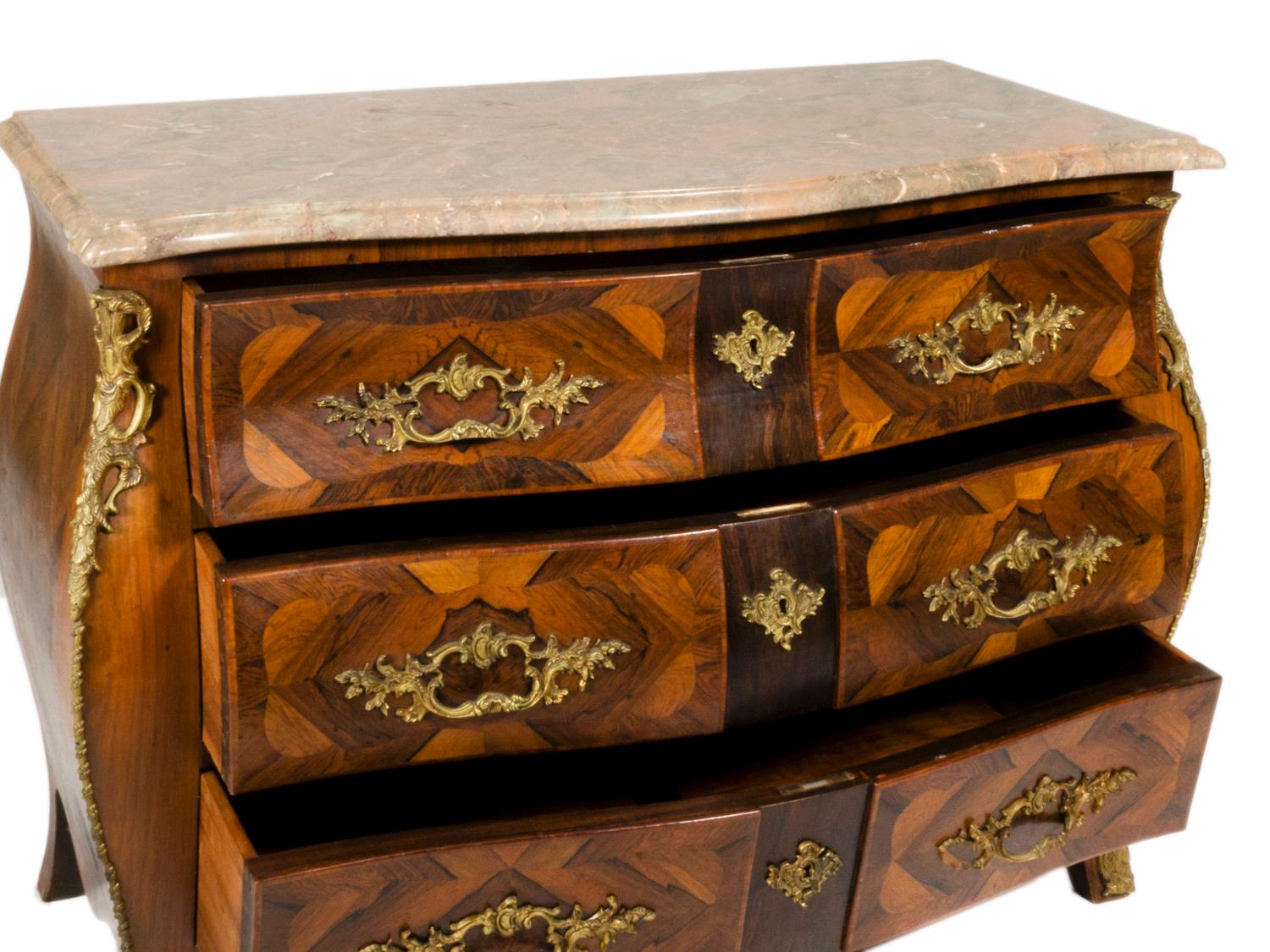 Questa cassettiera bombe è stata progettata nel classico stile francese Luigi XV e vanta uno splendido piano in marmo intarsiato, completo di intarsi e di una graziosa ferramenta in bronzo. 

Gli eleganti bordi smussati del marmo si abbinano