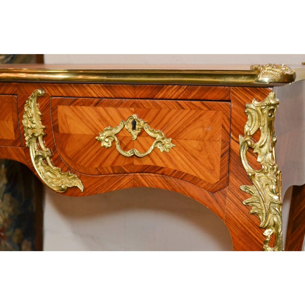 Superior quality small-scaled early 20th century French Louis XV style kingwood and leather top writing table or bureau plat with shaped top. Ornately mounted with gilt bronze acanthus leaf appointments and inset with three drawers. The entire on