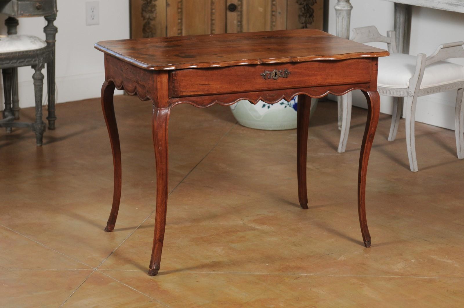 A French Louis XV cherry table from the Rhône Valley, with long drawer and cabriole legs. Born in France in the later years of the 18th century, this cherry table features a rectangular top with serpentine front, sitting above a long drawer. Raised