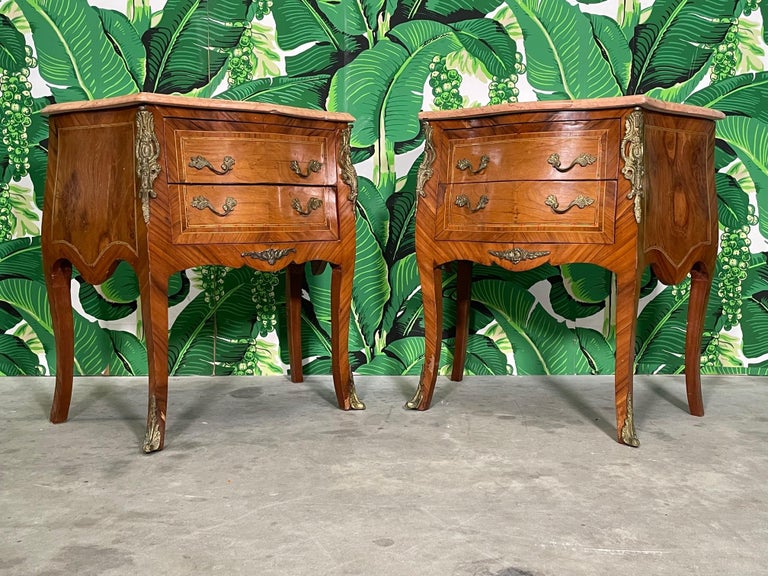 Pair of mid century King Louis XV style nightstands or end/side tables feature inlaid marquetry and beveled marble tops. Two drawers, cabriole legs, and mounted ormolu detailing. Good condition with imperfections consistent with age. May exhibit