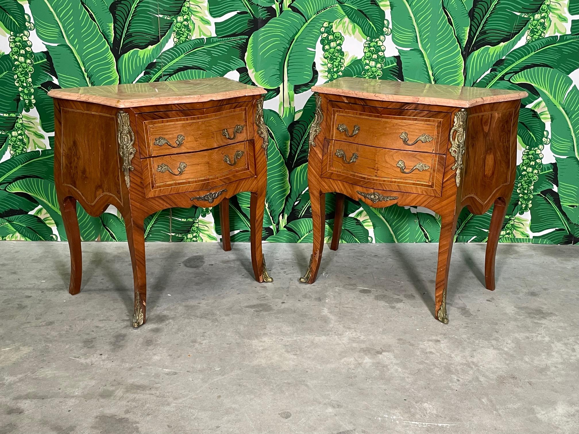 Pair of midcentury King Louis XV style nightstands or end/side tables feature inlaid marquetry and beveled marble tops. Two drawers, cabriole legs, and mounted ormolu detailing. Good condition with imperfections consistent with age. May exhibit