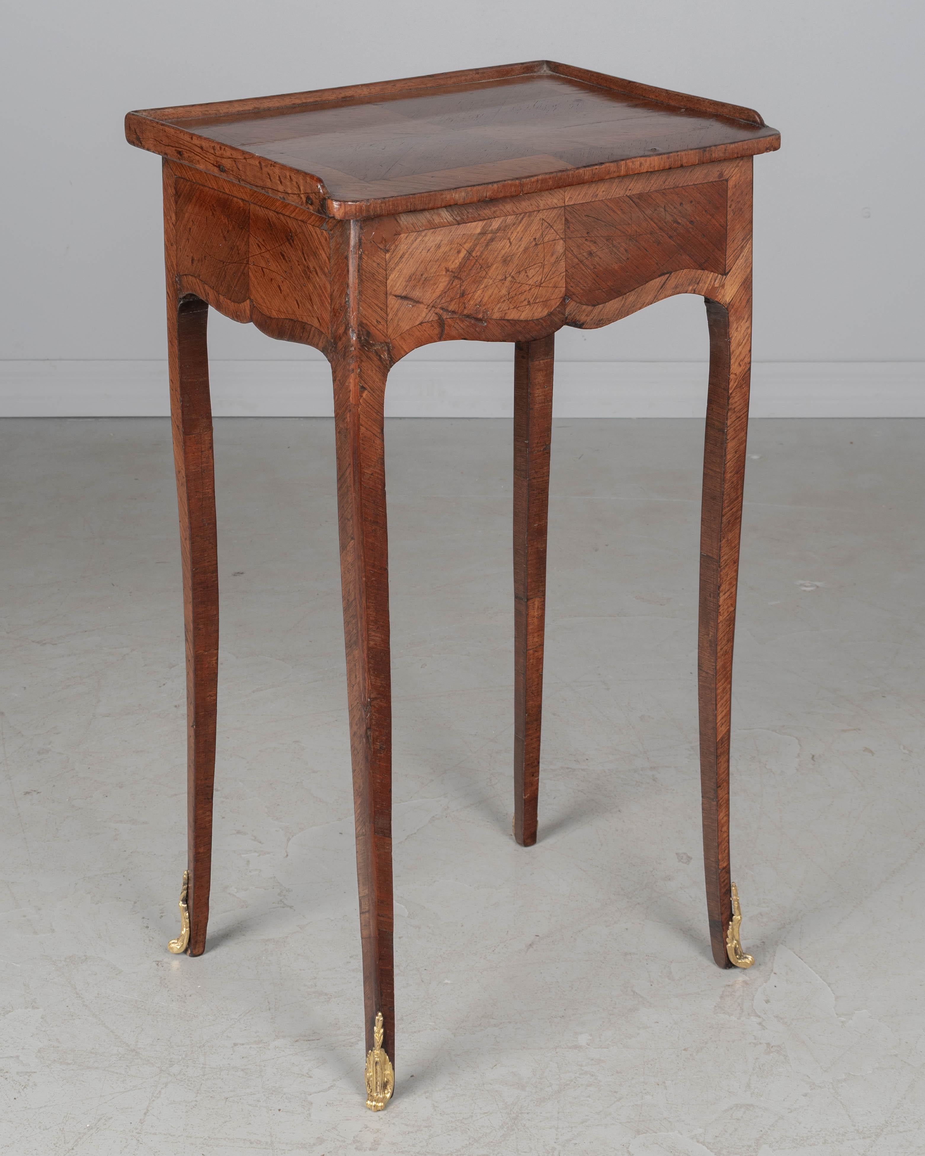 Table à écrire ou table d'appoint en marqueterie de style Louis XV-XVI du début du XIXe siècle. En placage de noyer et d'acajou. Tiroir simple à queue d'aronde avec petit bouton en bronze sur le côté droit. Pieds hauts, minces et incurvés avec