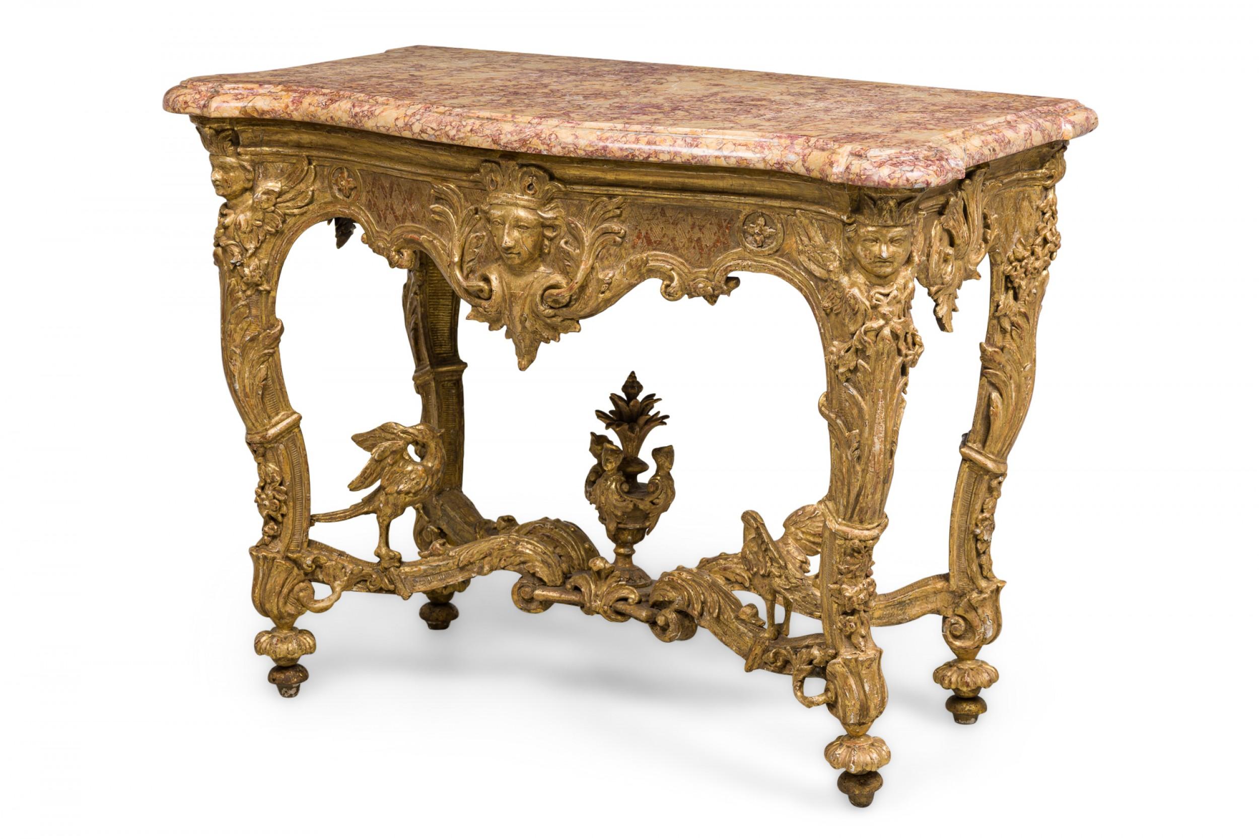 French Louis XV console table with an ornately carved giltwood base with figural designs and topped with a shaped beige, yellow, and blush marble top.