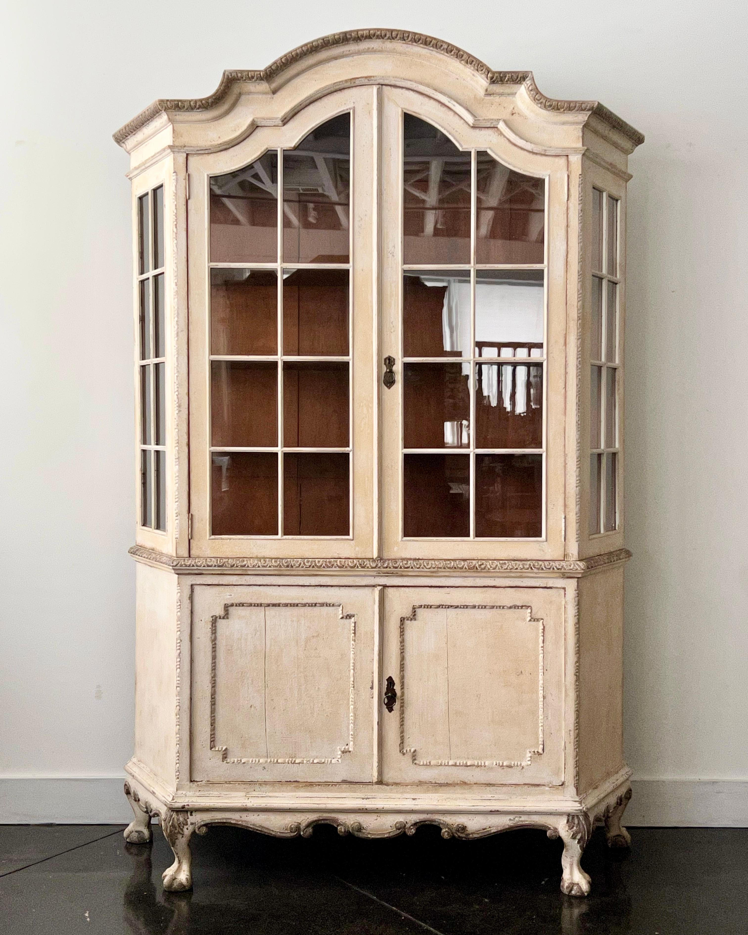 The 19th century glass-fronted bookcase /display cabinet of the Louis XV manner in painted walnut wood with a Chapeau de Gendarme crown. 
 Double glass doors open to give access to the shelved interior, the three shelves visible through the panes