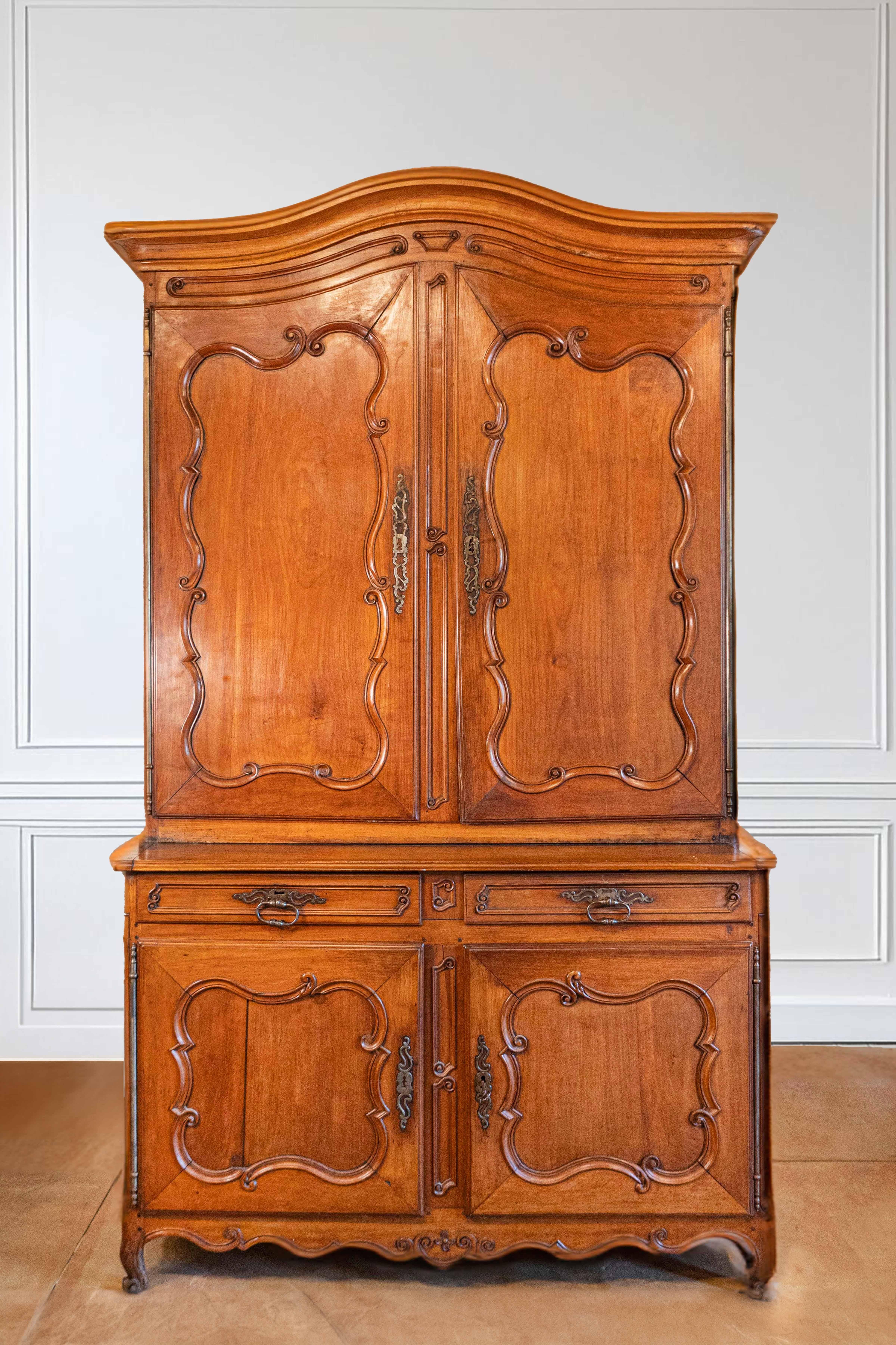 A French Louis XV period cherry buffet à deux-corps from the mid-18th century with original hardware. This French cabinet features a bonnet top surmounting two doors with carved panels and delicate c-scrolls. These small scrolled motifs are repeated