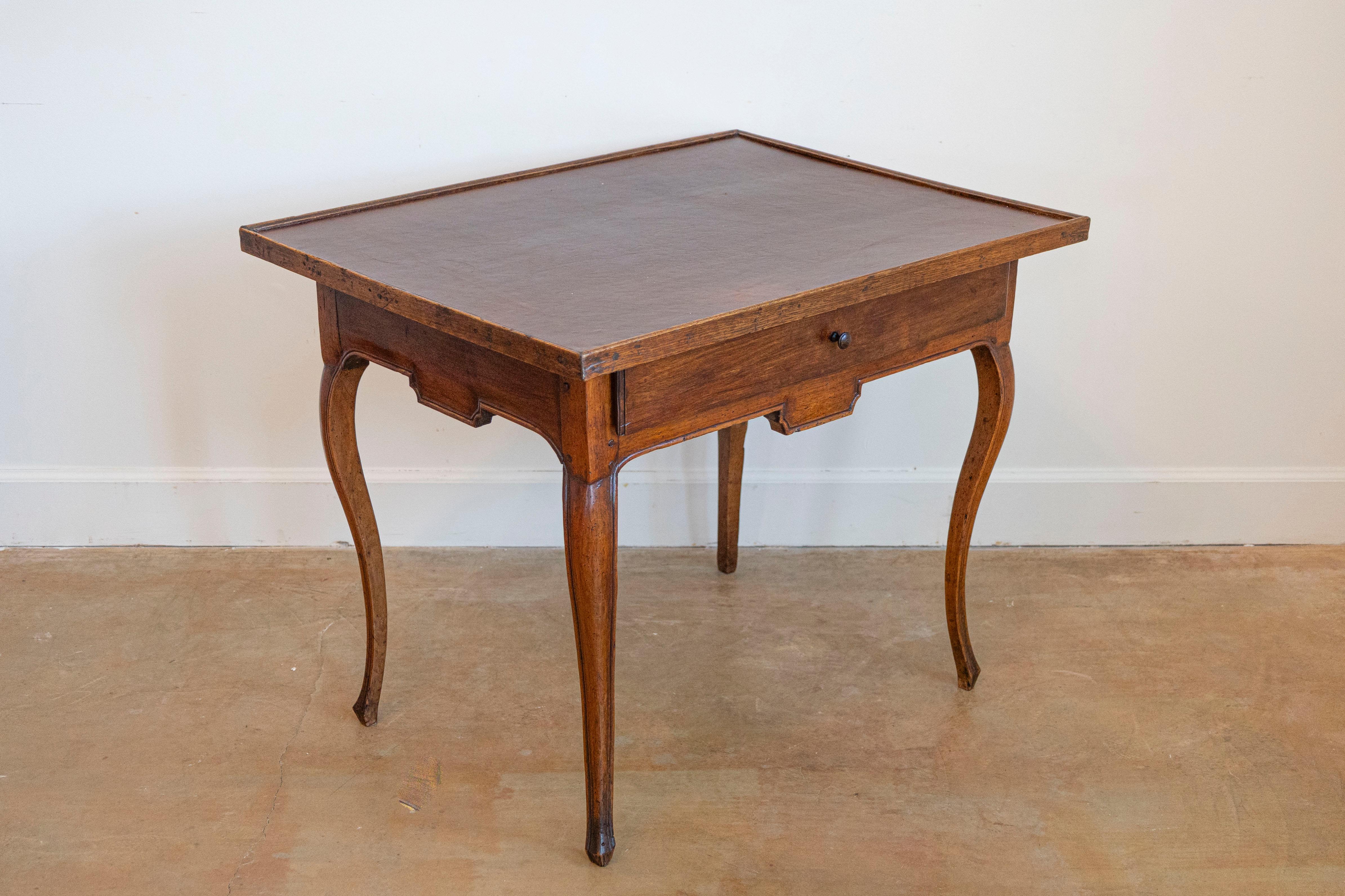 Mesa de juego francesa de época Luis XV del siglo XVIII con tablero de cuero marrón, un solo cajón, delantal tallado y patas cabriolé. Esta exquisita mesa de juego francesa de época Luis XV, fabricada en el siglo XVIII, es un testimonio del encanto