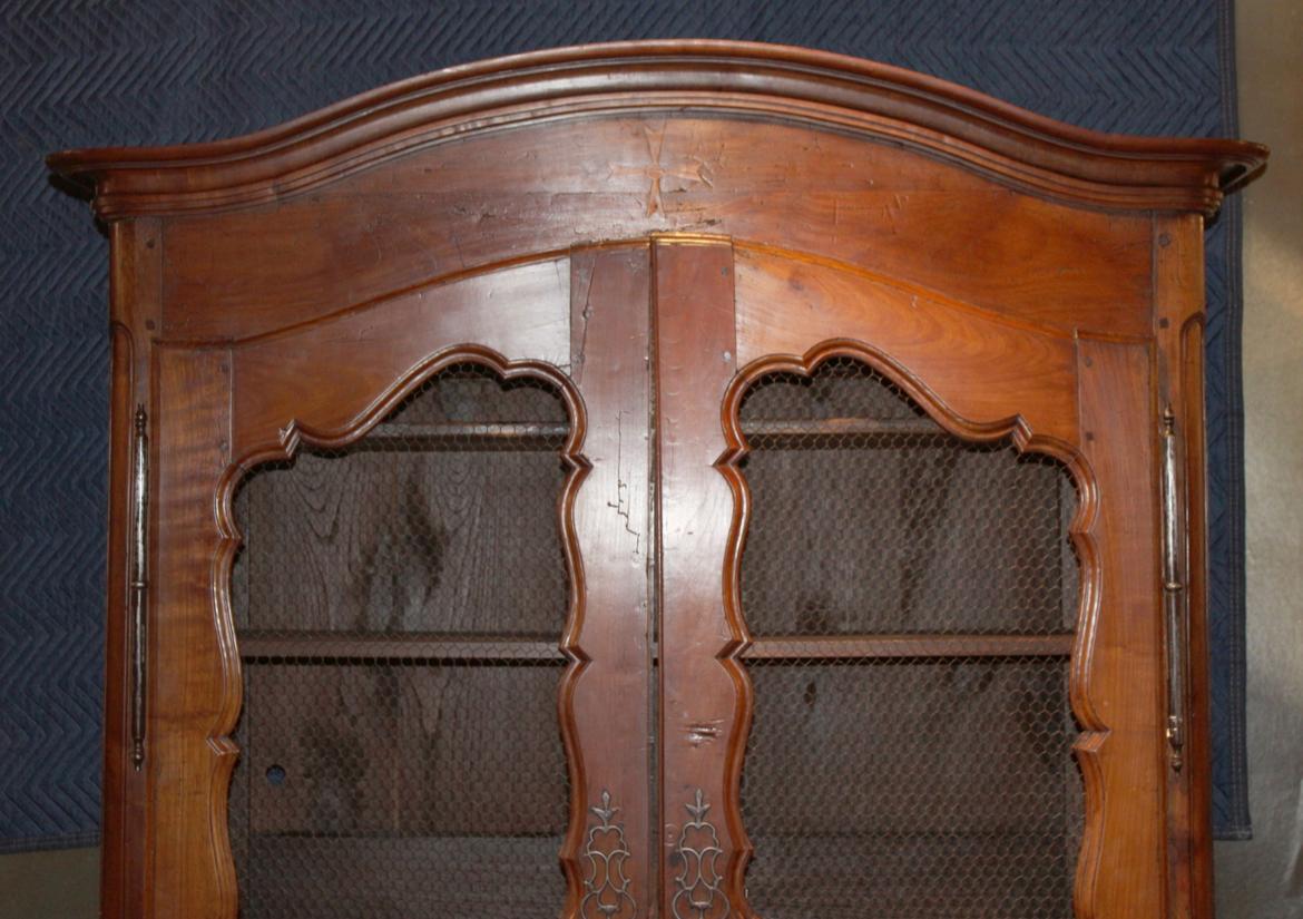 Un armadio francese di epoca Luigi XV in ciliegio, ora convertito in libreria con pannelli in filo di ferro antico incastonati nella coppia di porte ad arco.  Croce di Malta nel pannello ad arco sopra le porte. 