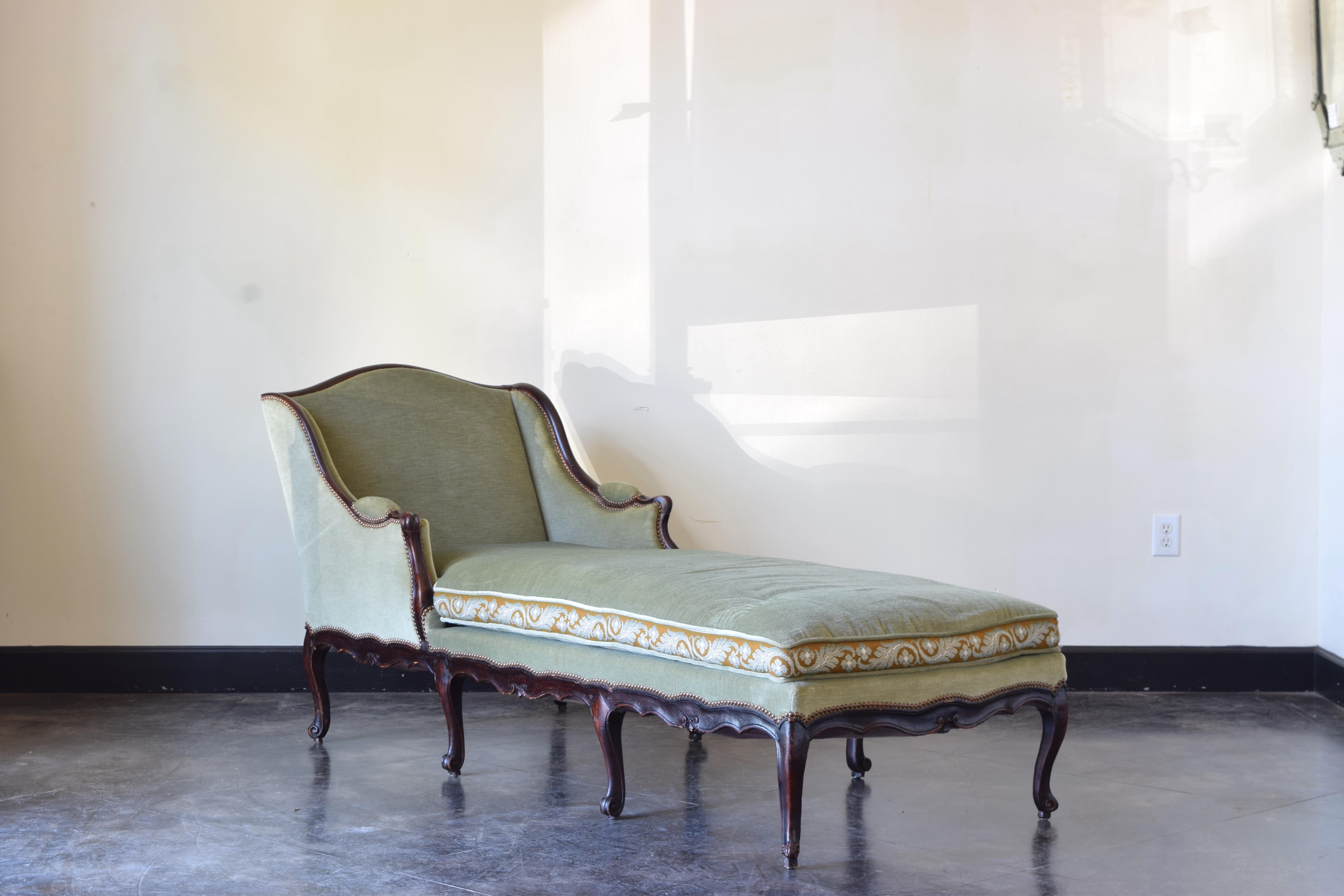 Having a shaped and leaning backrest with bergere sides and padded armrests, with scalloped carved apron and eight cabriole carved legs, upholstered in pale green velvet, exceptional for its width and length, very comfortable