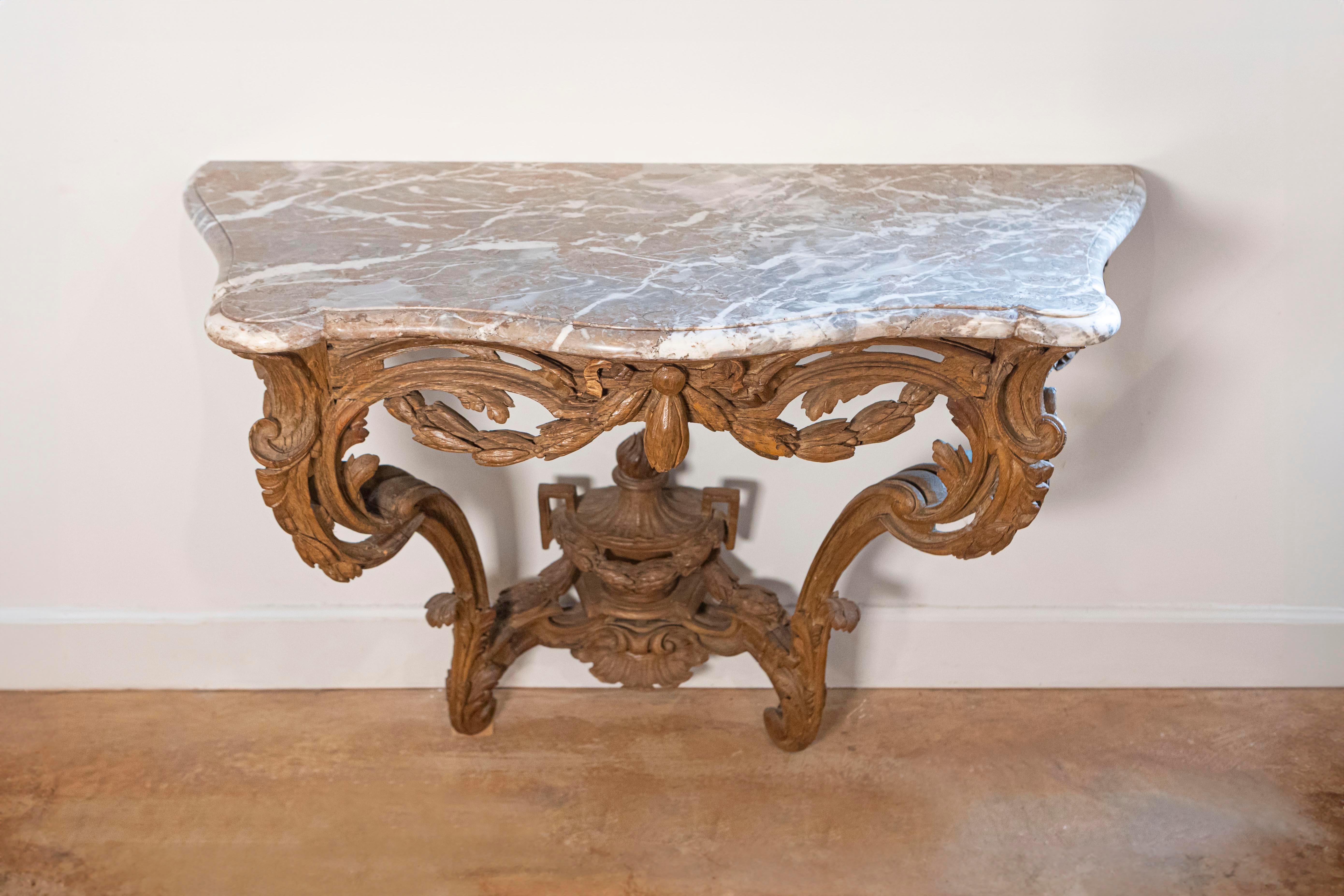 A French Louis XV period carved wood console table with marble top from the mid-18th century. This French console table, circa 1760 features a shaped veined marble top sitting over an exquisitely carved wooden base. The center of the apron showcases