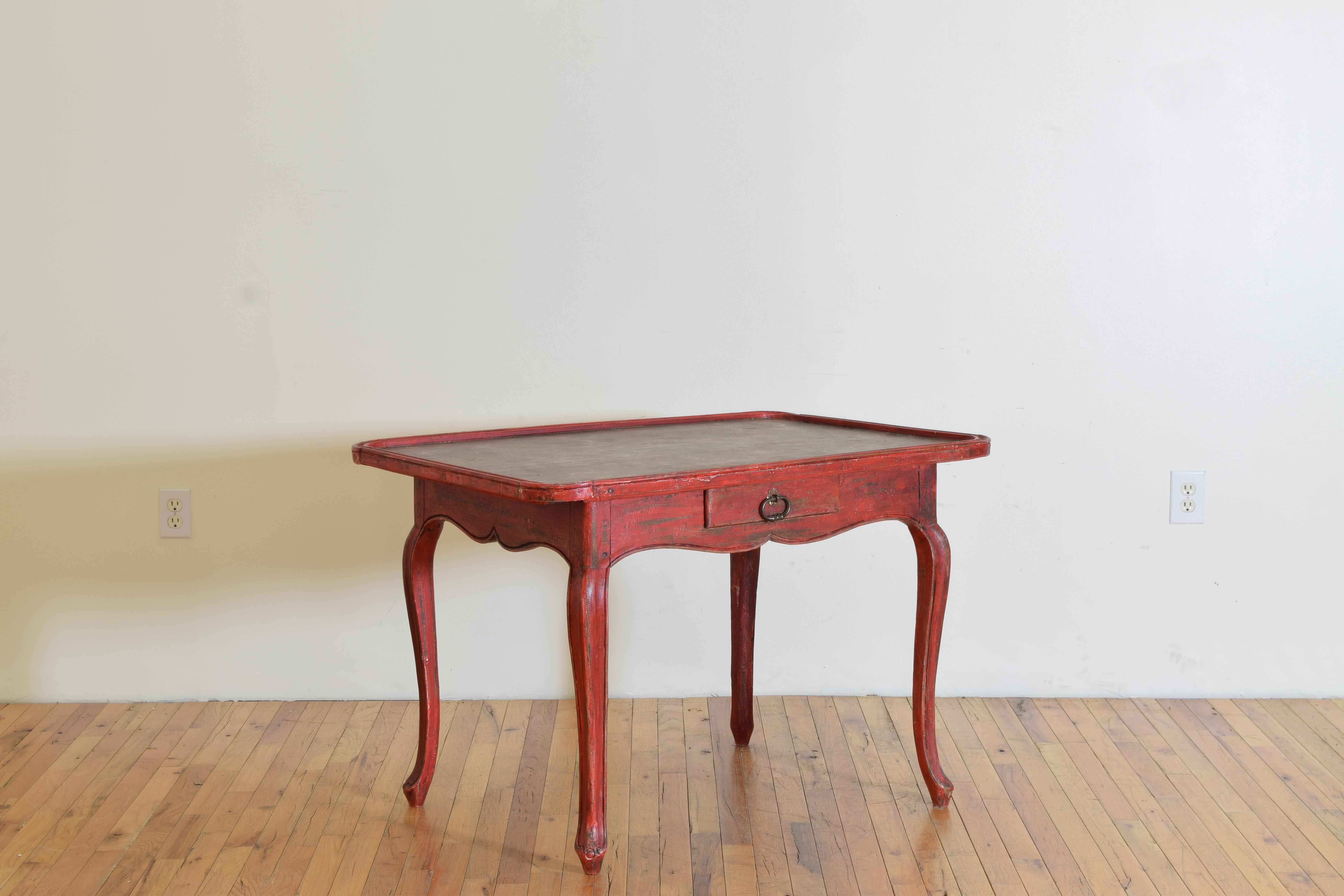 Painted in a faded red color and having a rectangular shaped top with rounded corners and a raised molding, the top likely previously covered in fabric atop a conforming case housing one drawer with an iron pull, raised on cabriole shaped legs