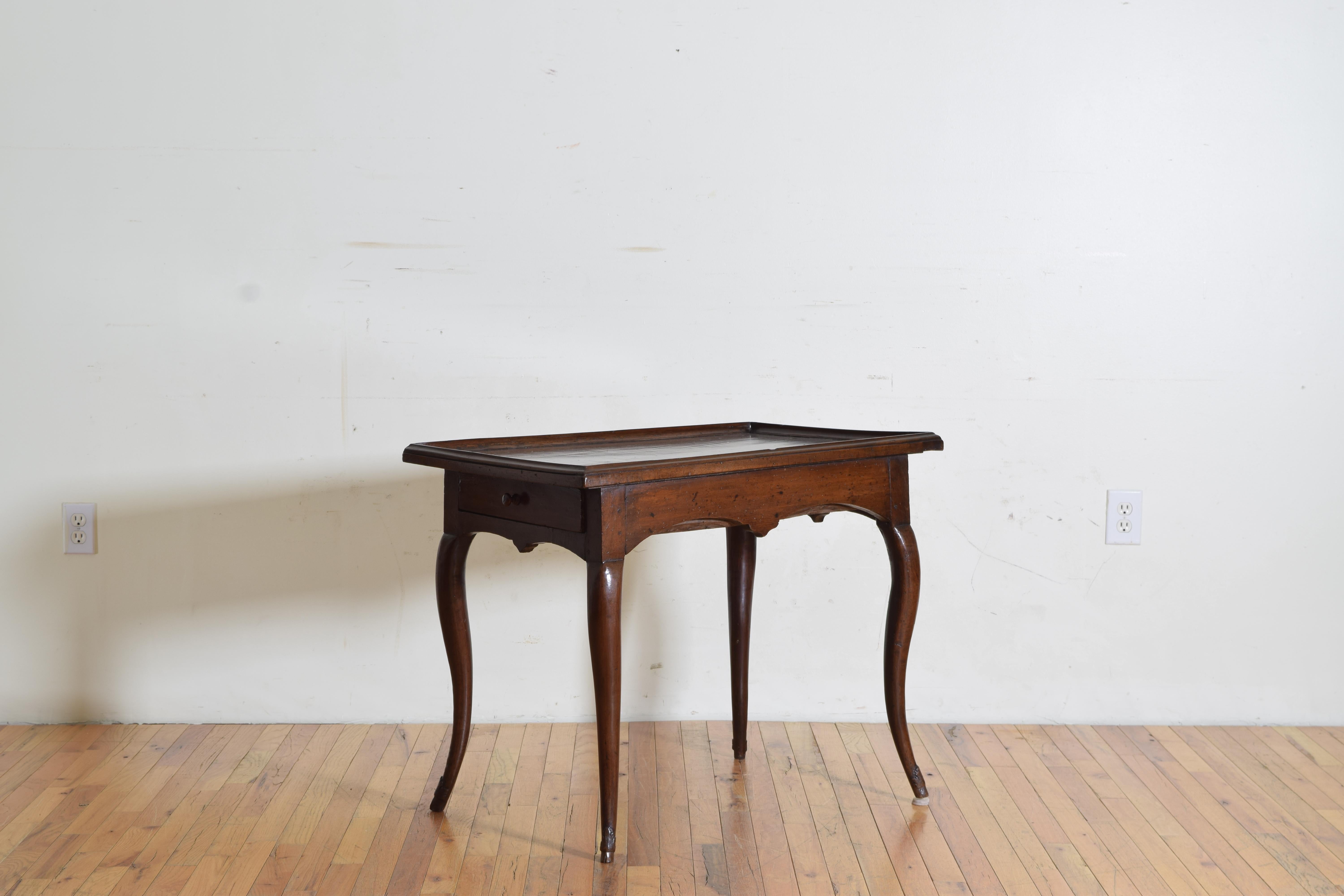 The rectangular top with a thick galleried edge above a conforming case housing two-side drawer each having a wooden pull, the table raised on tapering cabriole legs ending in small hoof feet with carved “feathers” above them.