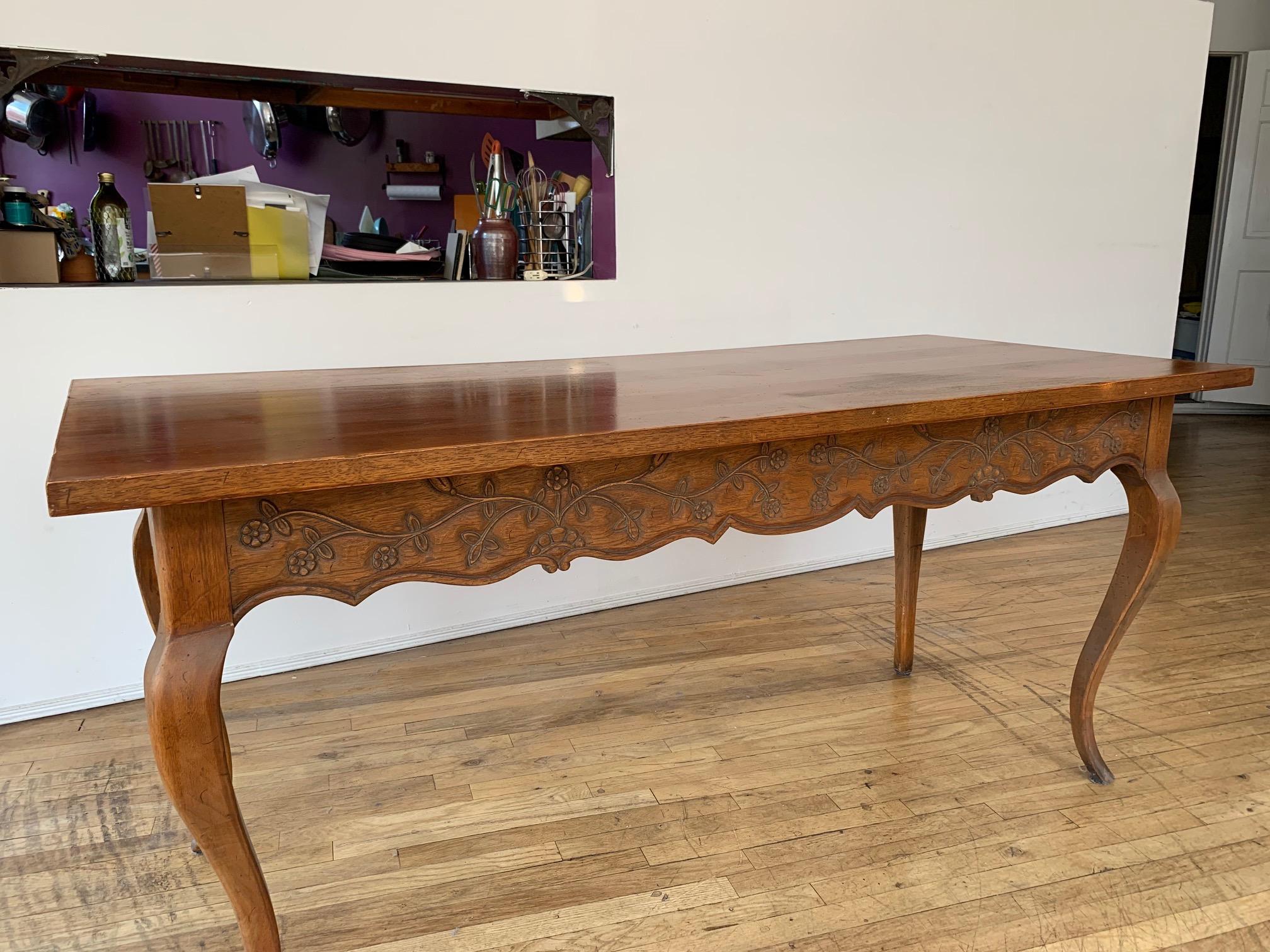 French Louis XV Provincial style carved walnut dining/refectory table.
Hand-carved foliage along the length on each side of the table. One side with two drawers. Sitting on cabriole legs. This is a beautiful provincial style piece with light wear to