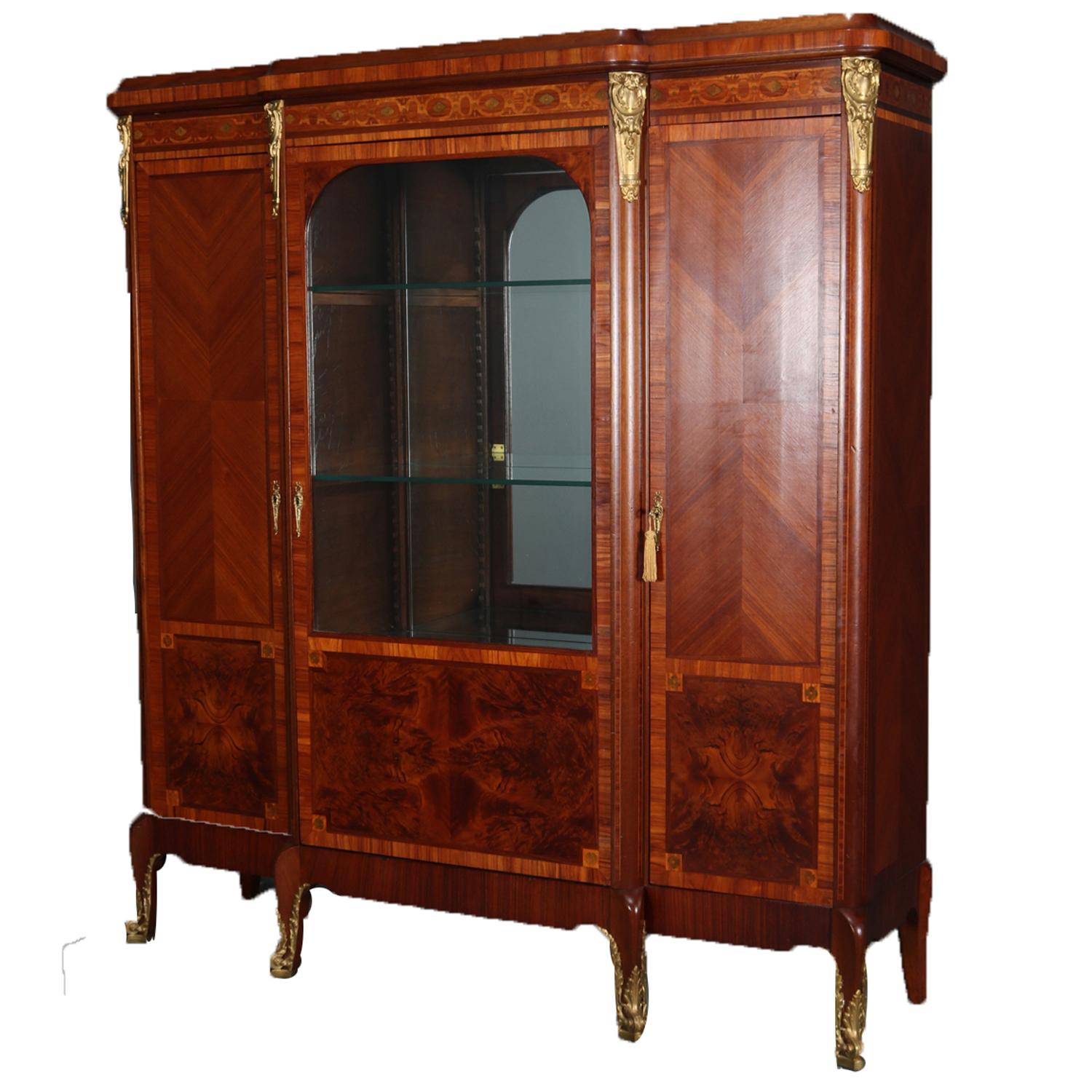 French Louis XV school flame mahogany locking china display cabinet features crossbanded and inlaid frieze over central glass door opening to mirror back and shelved interior and flanked by blind doors with book matched and burl elements opening to