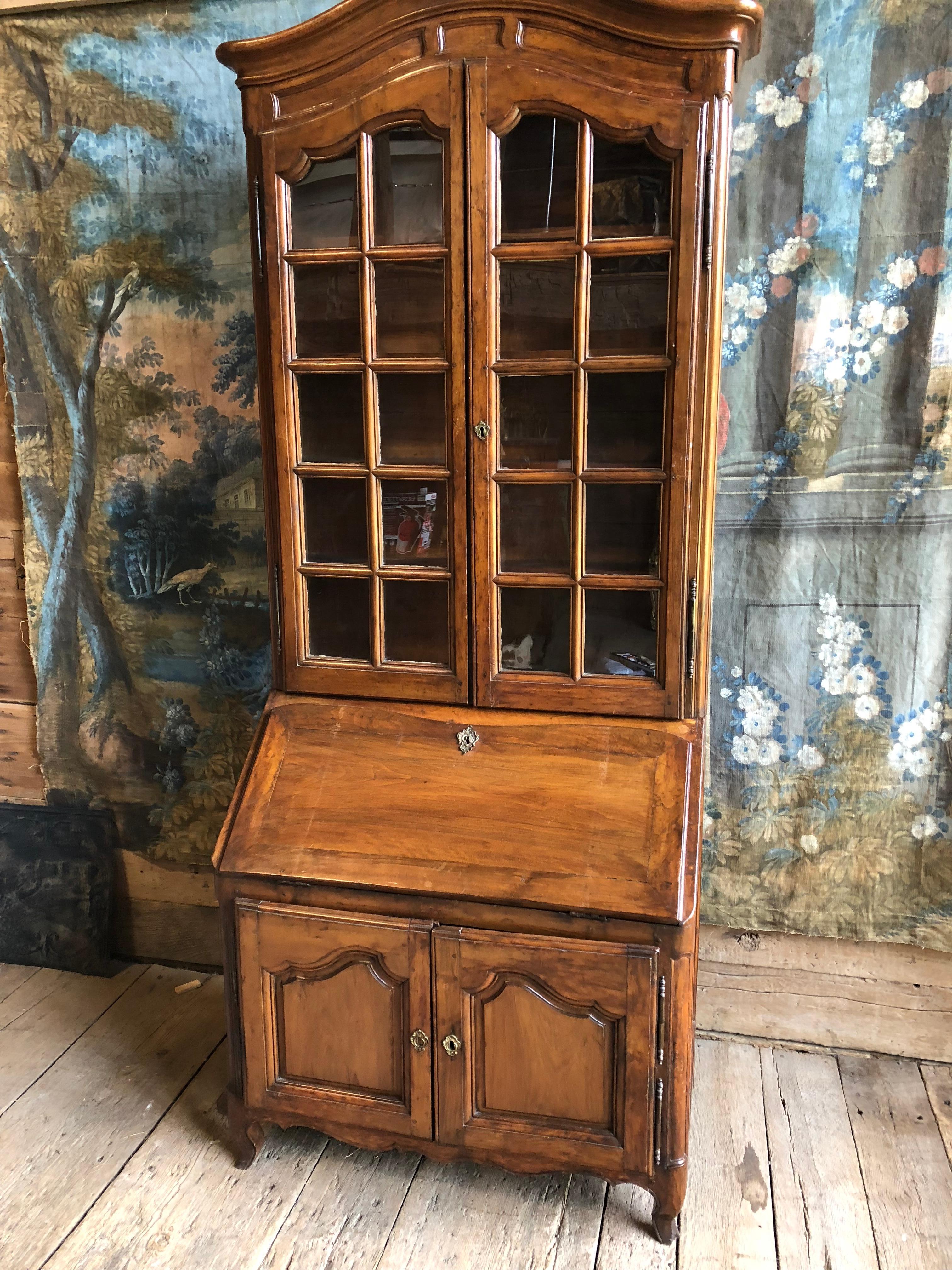 A Louis XV period secretaire with upper bookcase, French, circa 1760, with an arched bonnet top biblioteque with glazed doors, over a slant-front desk with fitted interior, a lower 2-door cabinet on short cabriole feet.