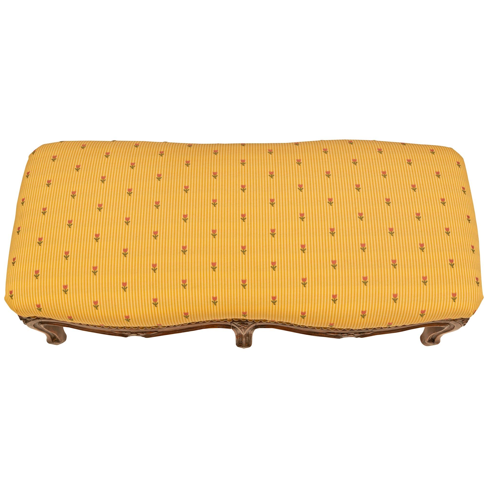 Charmant banc bas français de style Louis XV, datant du milieu du XIXe siècle. Le banc est surélevé par six pieds cabriole surmontés de fleurs merveilleusement et richement sculptées. Le tablier présente un motif festonné parmi d'autres sculptures