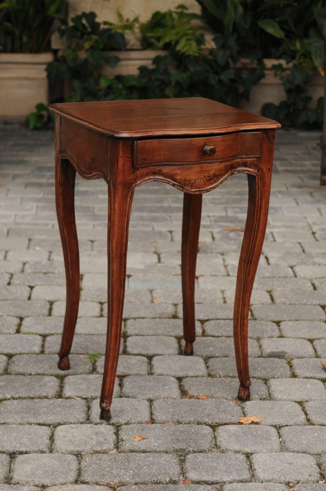 A French Louis XV style walnut side table from the early 19th century, with single drawer and scalloped apron. Born during the first French Empire, this delicate walnut table features a rectangular planked top with beveled edges and serpentine