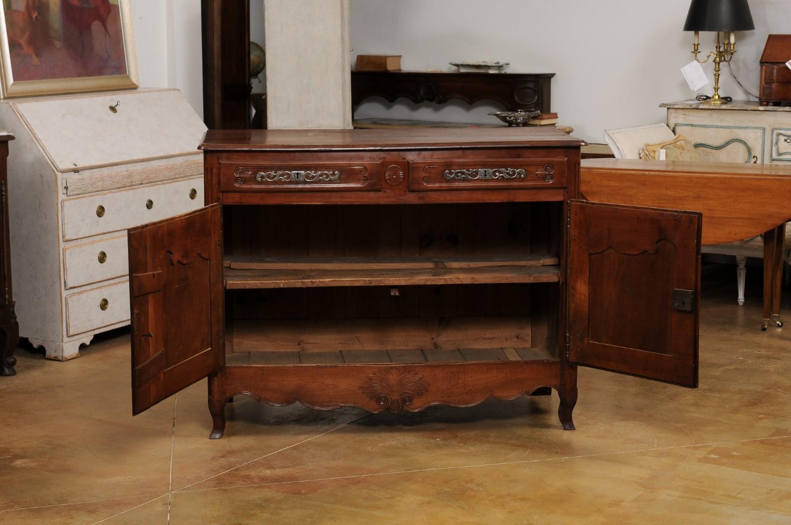 A French Louis XV style walnut buffet from the Mid-19th Century with two drawers, two carved doors and Rococo style hardware. Created in France during the 1850s, this walnut buffet showcases the stylistic characteristics of the King Louis XV era.