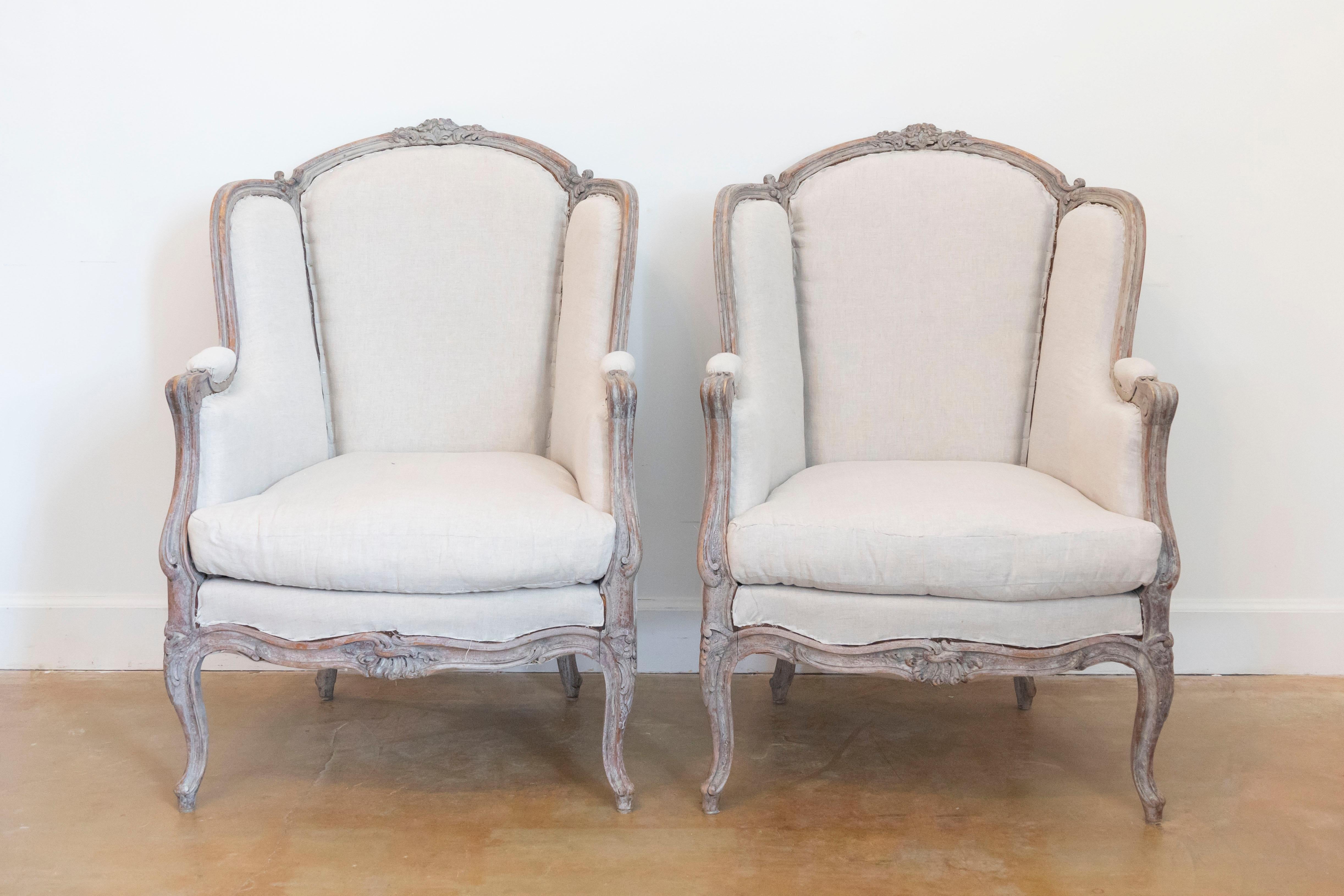 A pair of French Louis XV style painted wood bergères à oreilles chairs from circa 1880 with carved floral motifs, cabriole legs and used upholstery. This exquisite pair of French Louis XV style bergères à oreilles, dating back to circa 1880,