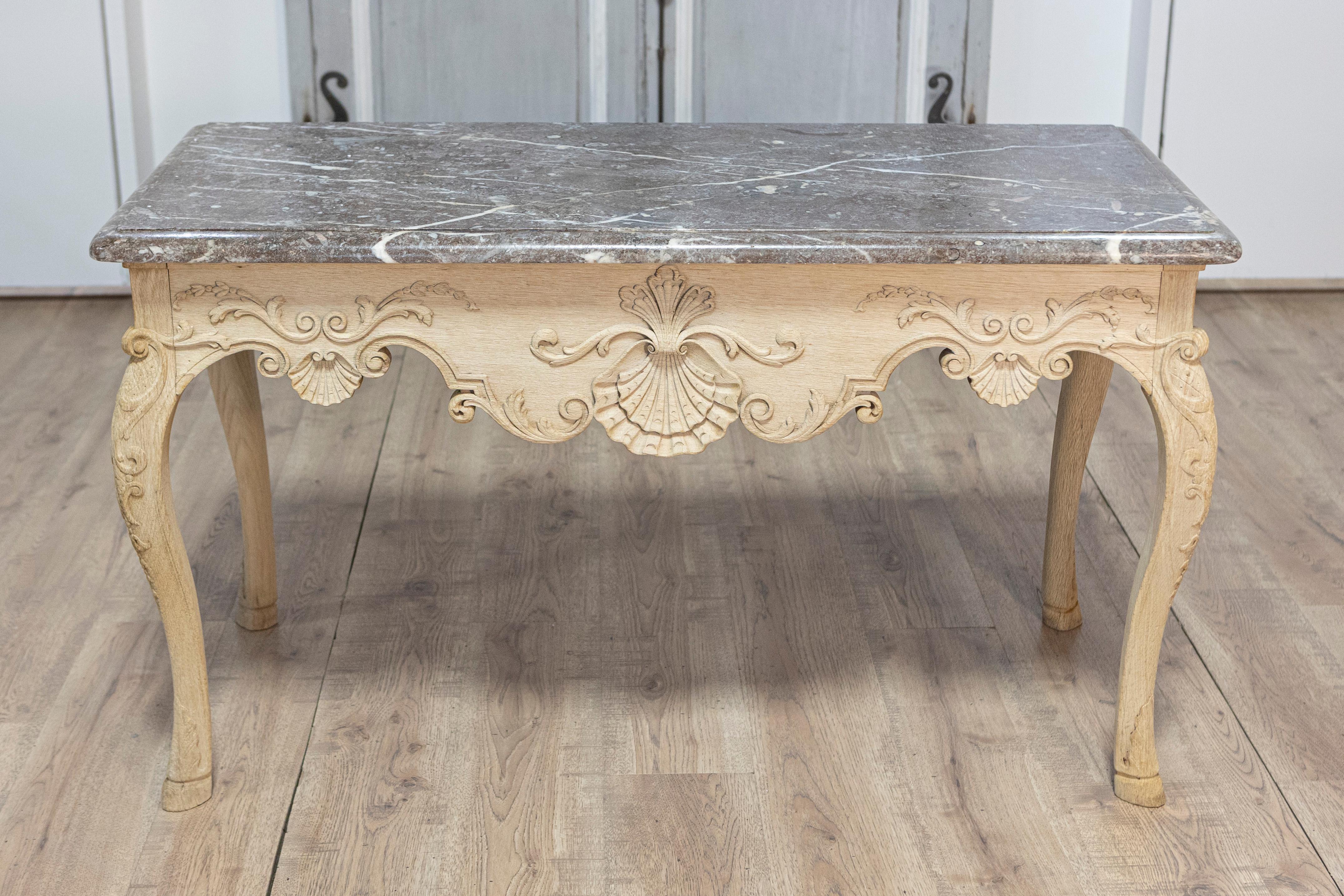 Consola francesa de madera blanqueada de estilo Luis XV de hacia 1890 con tapa de mármol gris, delantal tallado y patas cabriolé. Fabricada en Francia hacia 1890, esta elegante consola de madera blanqueada estilo Luis XV cautiva por su elegante