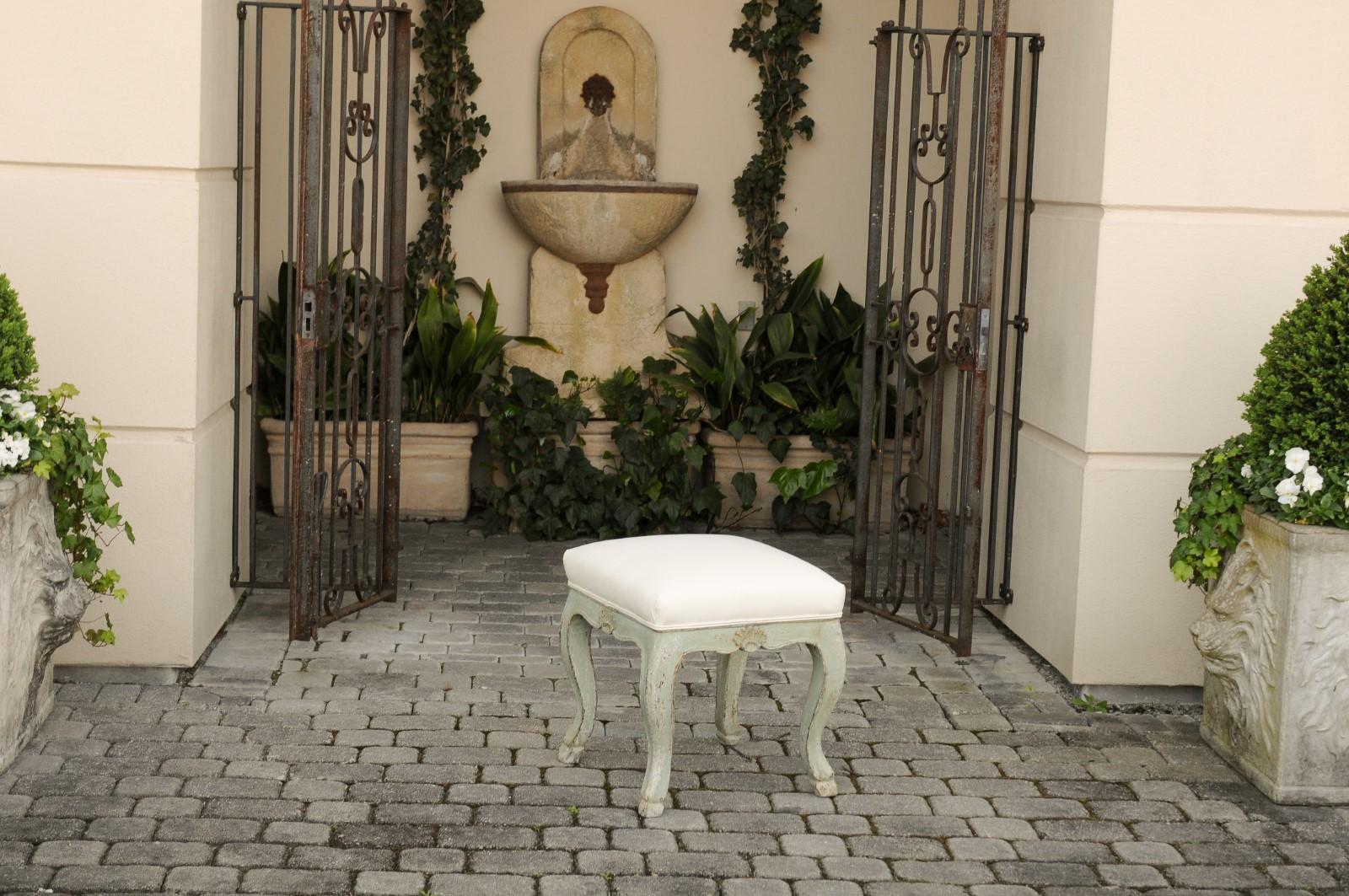 A French painted Louis XV style stool from the late 19th century, with cabriole legs, distressed finish and hoofed feet. Born in France during the Belle Époque era, this exquisite painted stool features a square seat, covered with a simple double