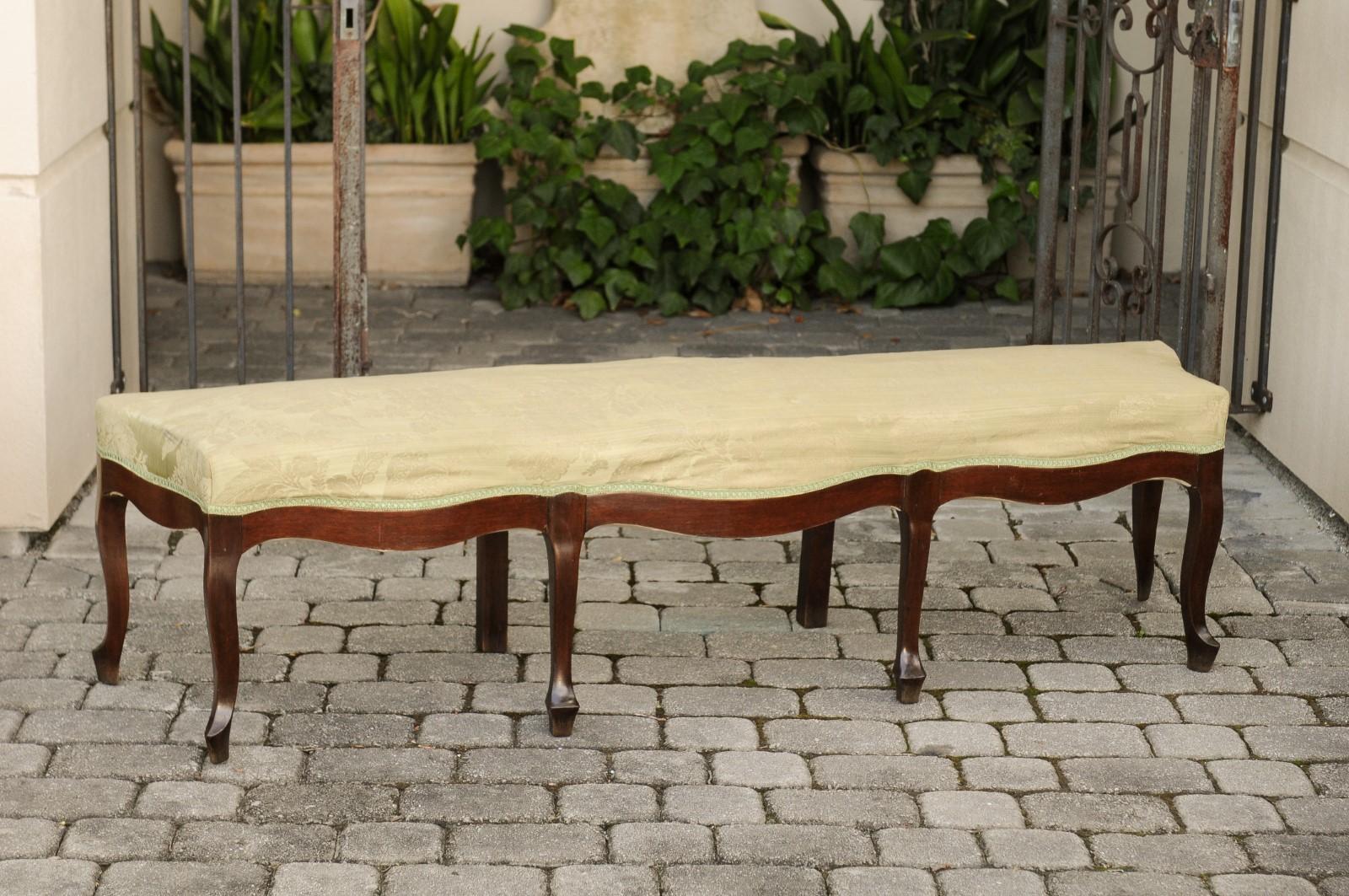 A French Louis XV style walnut bench from the early 20th century, with floral fabric and scalloped apron. Born in France during the Turn of the Century, this exquisite walnut bench features a rectangular serpentine top covered with a soft colored