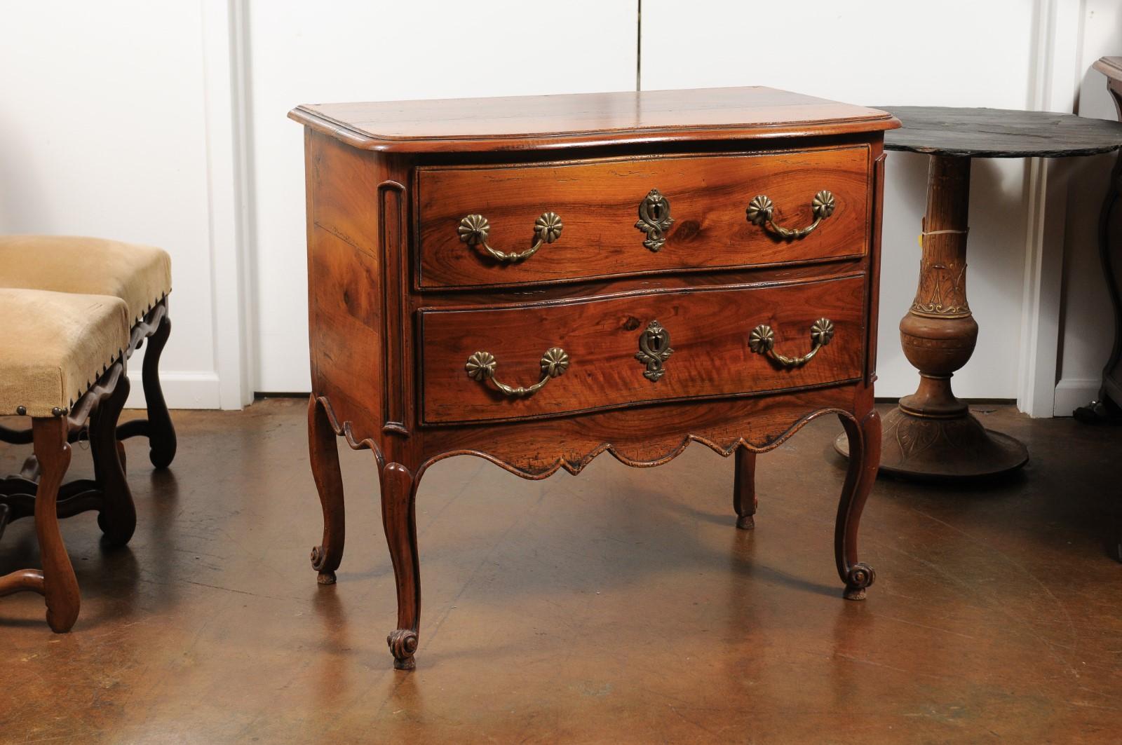 A French Louis XV style walnut two-drawer commode from the early 20th century, with scalloped skirt, cabriole legs and brass hardware. Born in France at the turn of the century during the Belle Époque era, this pretty commode features a rectangular