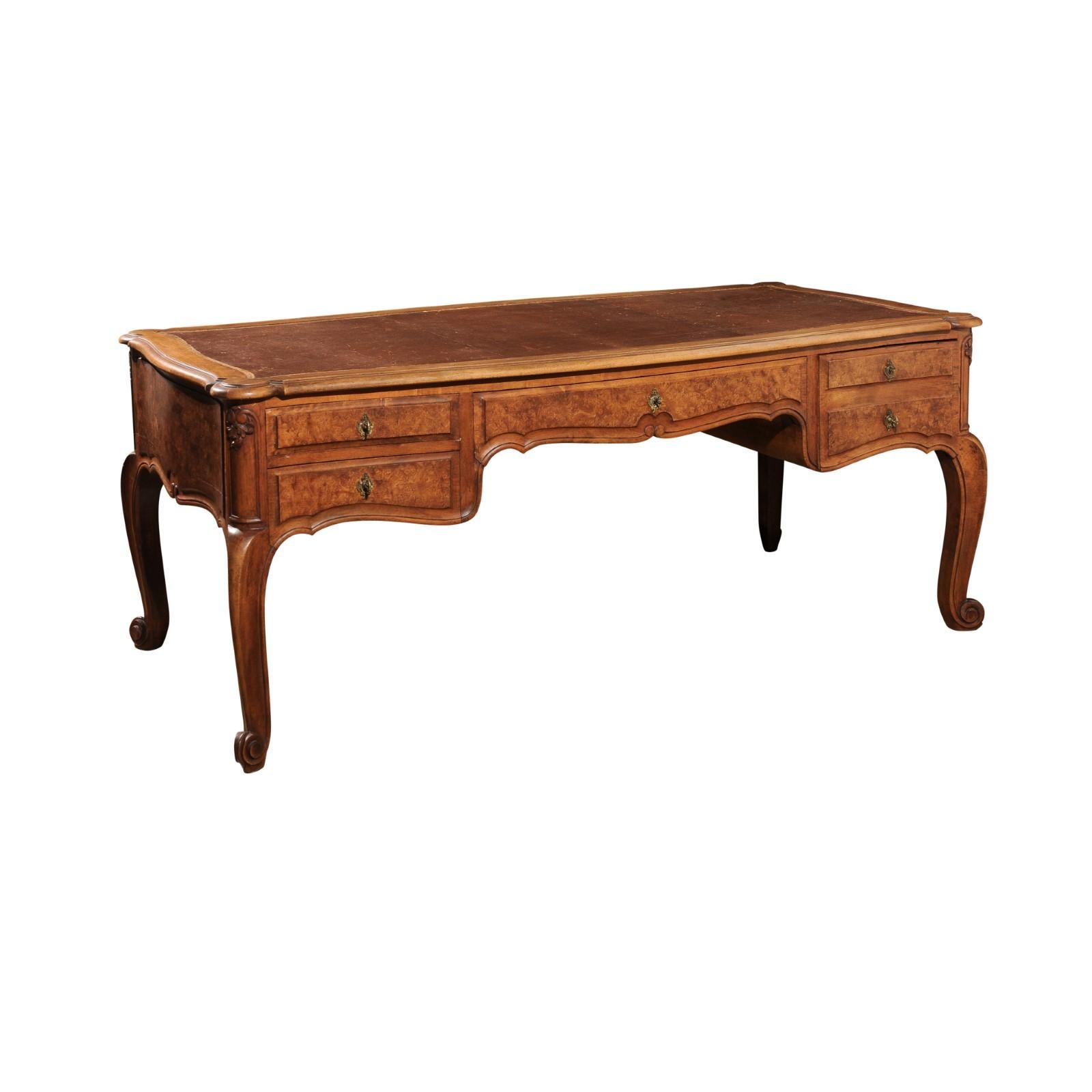 A Southern French Louis XV style 19th century burr walnut four-drawer desk from Avignon with leather top, foliage-carved décor and cabriole legs. Discover the grandeur and exquisite craftsmanship of this Southern French Louis XV style desk from the