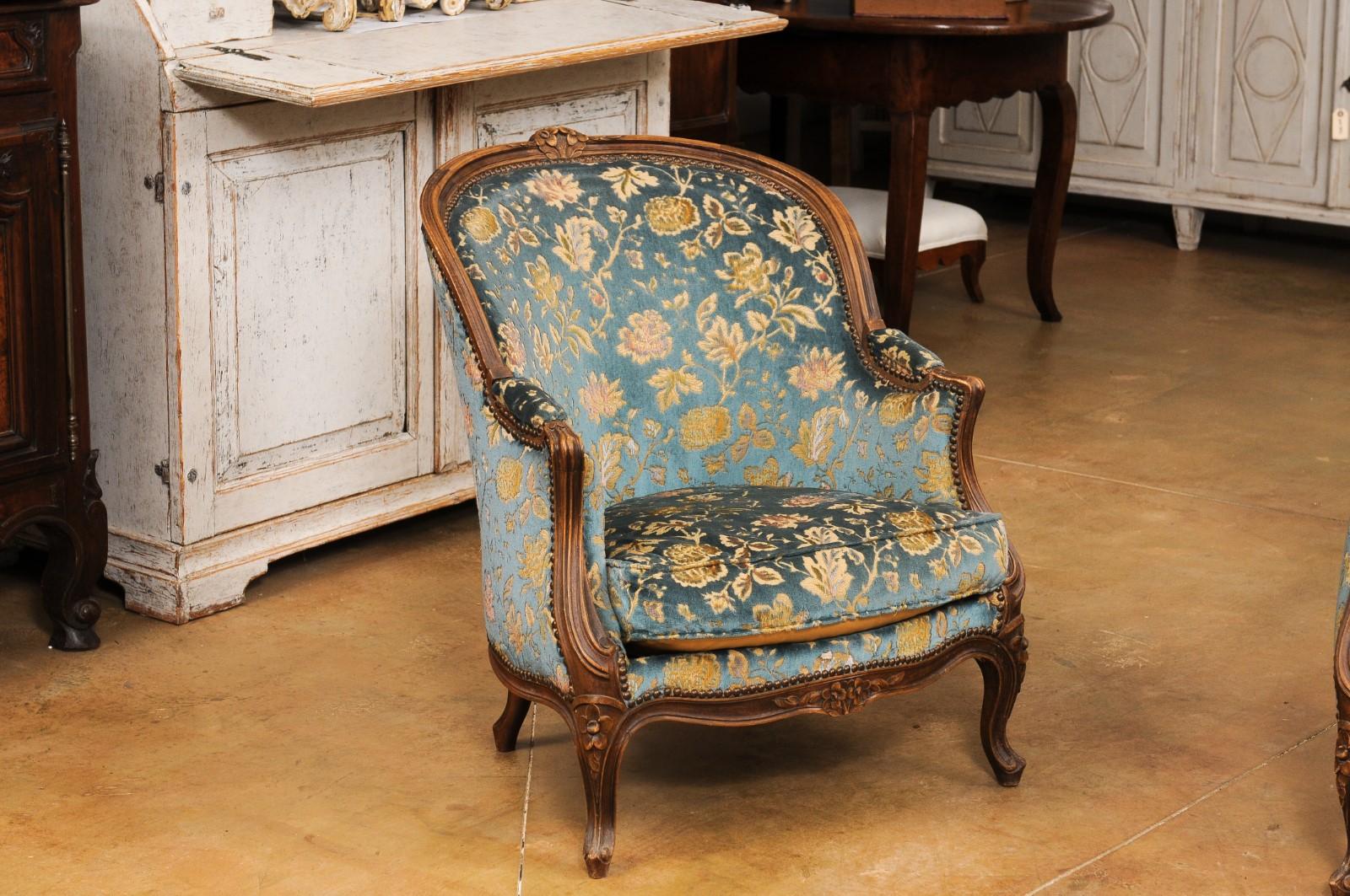 A French Louis XV style walnut bergères chair from the 19th century with carved crests, scrolling arms, floral carved apron, cabriole legs and floral upholstery. Enhance your living space with this exquisite French Louis XV style walnut bergères